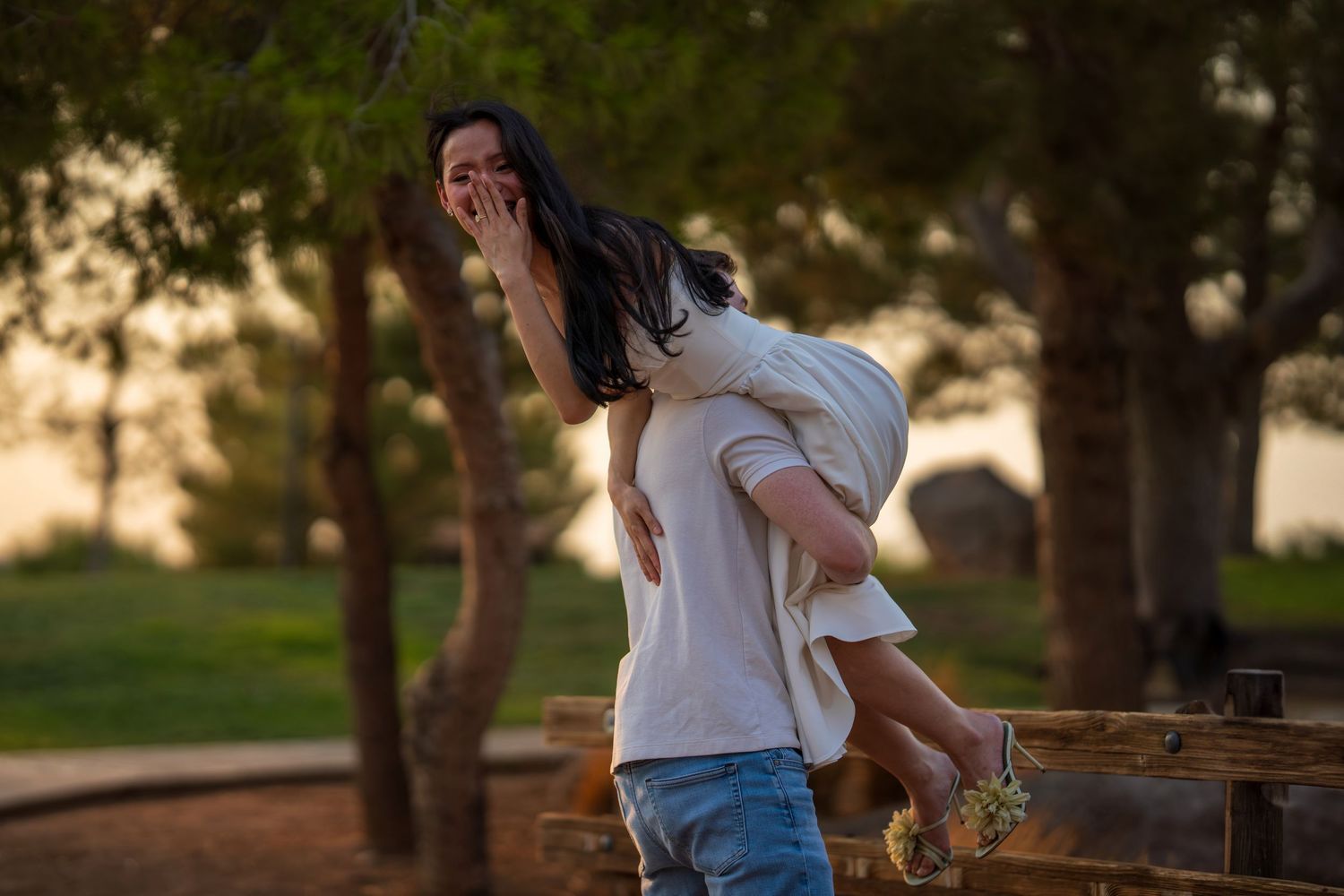 Man playfully carries laughing woman on his back in a sunny outdoor park setting.
