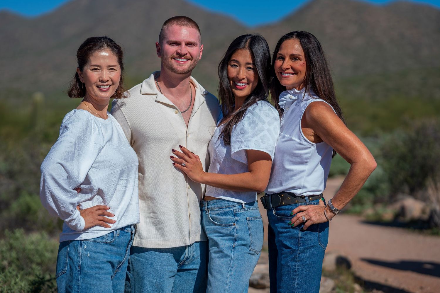 People in coordinated white shirts and denim stand together in a desert landscape with saguaro cacti.