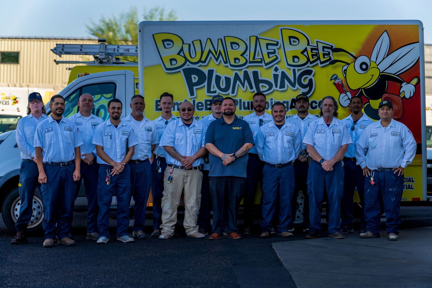 Staff gathering in front of yellow service vehicles with Bumble Bee Plumbing branding.