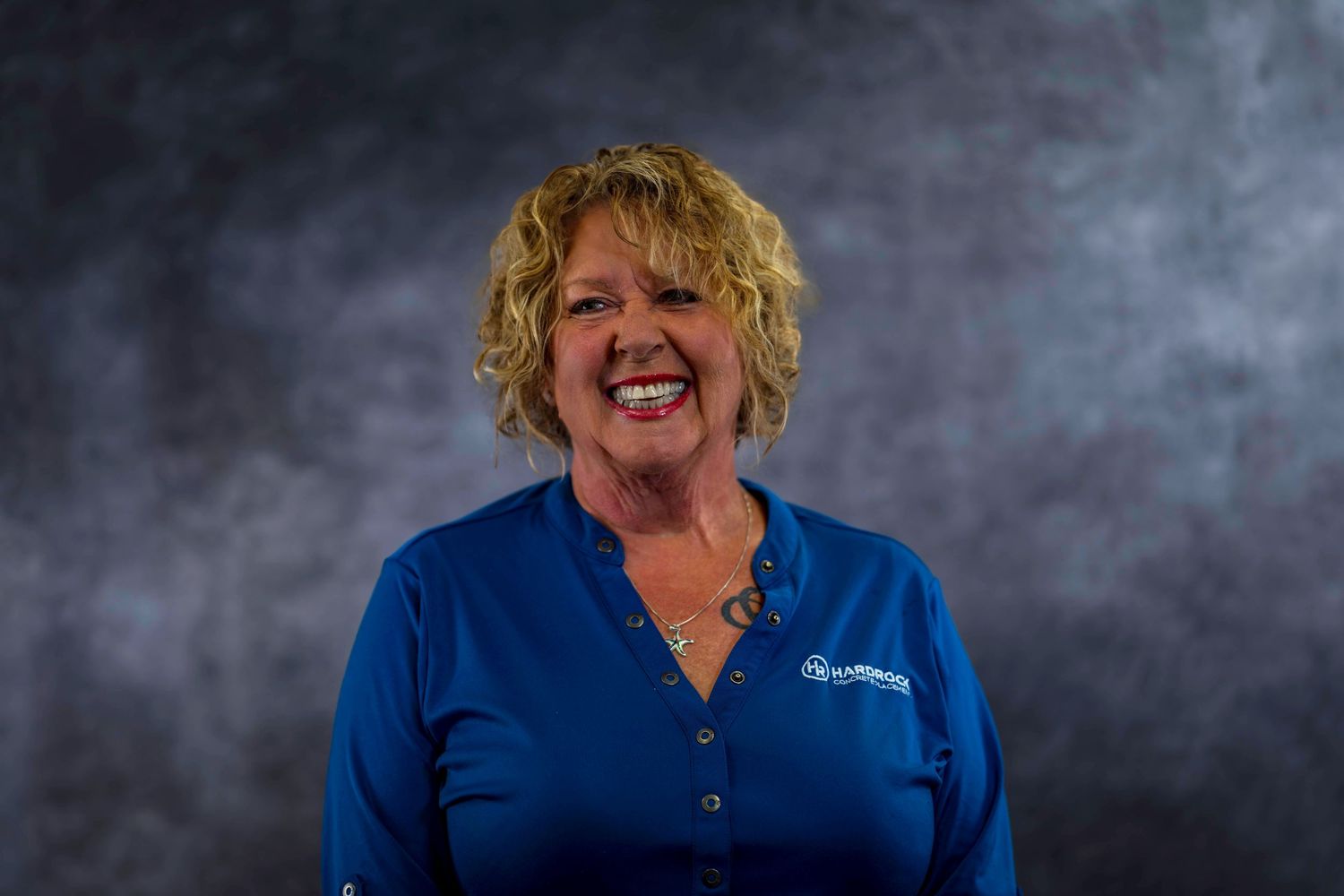 Cheerful employee portrait in blue company shirt against textured gray background.