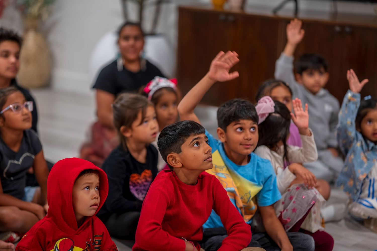 Children sitting on floor watching intently during performance with excited expressions.