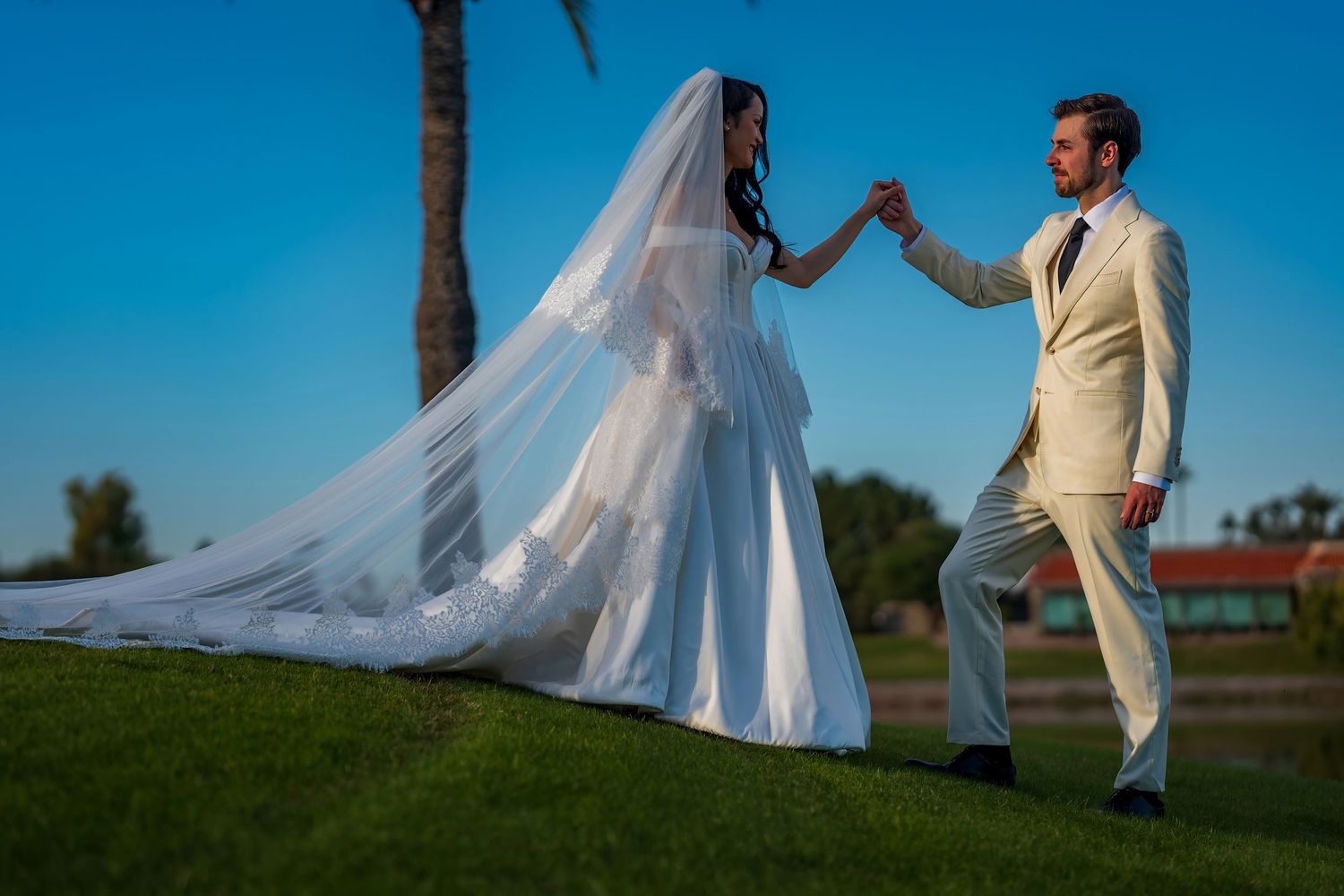 A couple poses for romantic wedding photos on a sunny day with palm trees in the background.