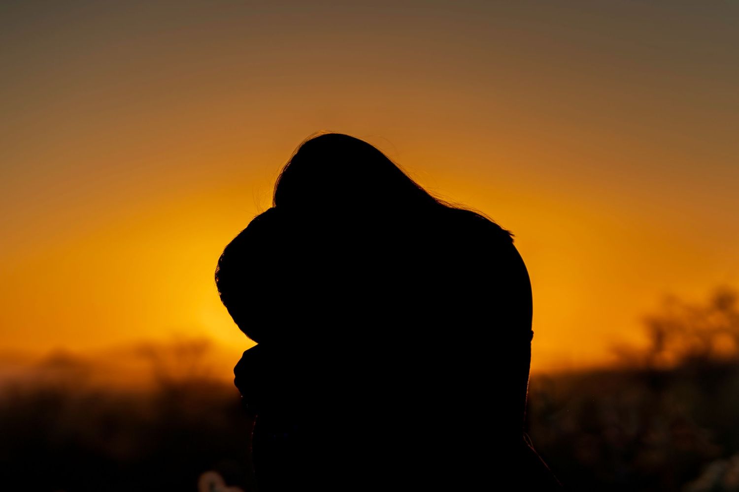 Silhouette of a couple embracing against a vibrant golden sunset sky with warm orange hues.