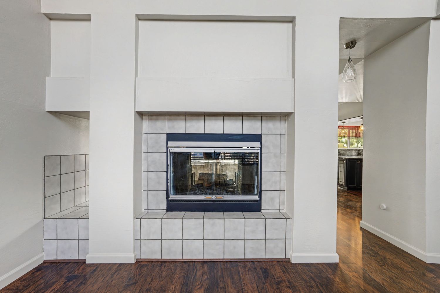 White tile fireplace with glass doors and dark hardwood floors in a bright living room.