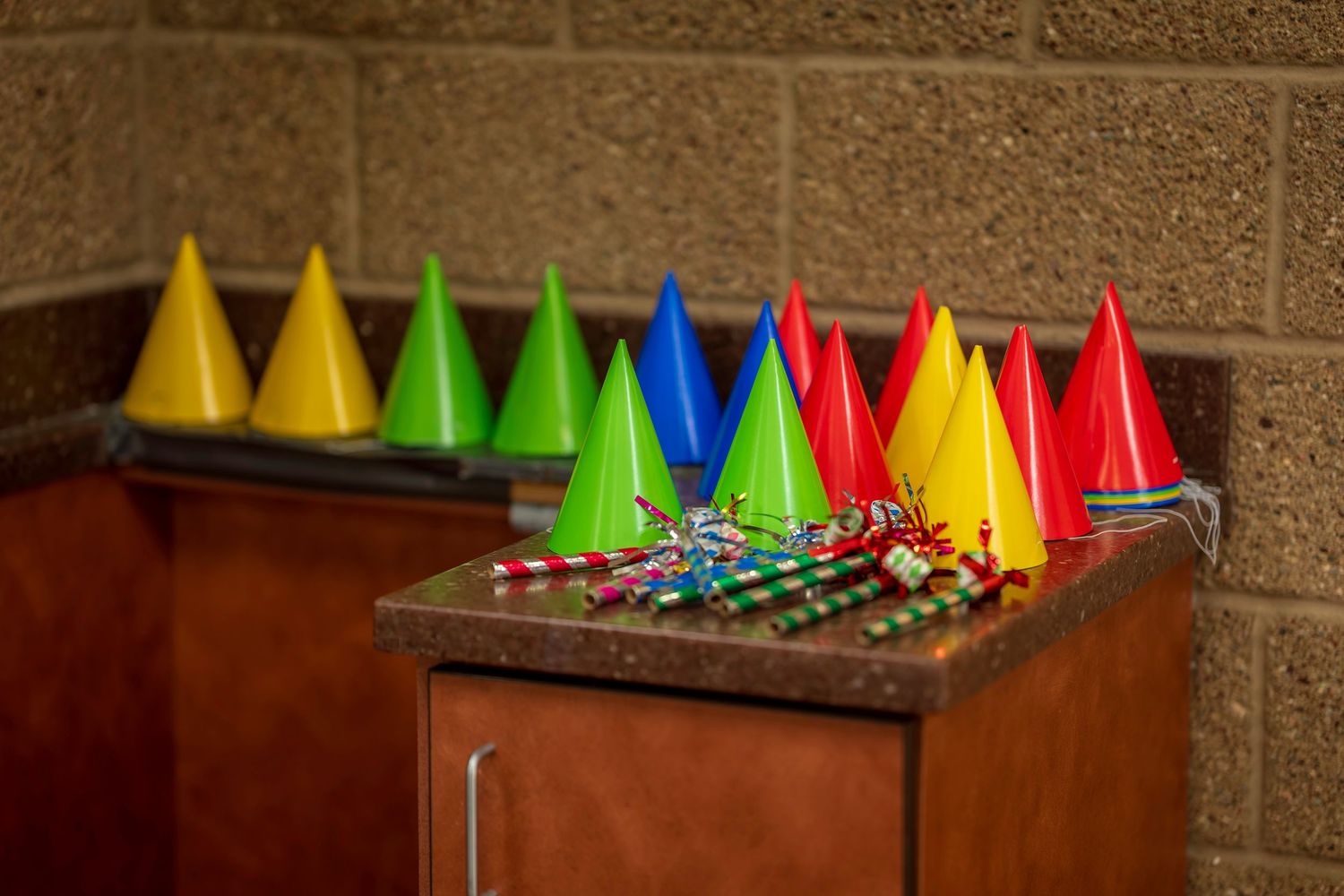Colorful party hats in red, yellow, green, and blue arranged on a wooden counter with festive curly straws nearby.