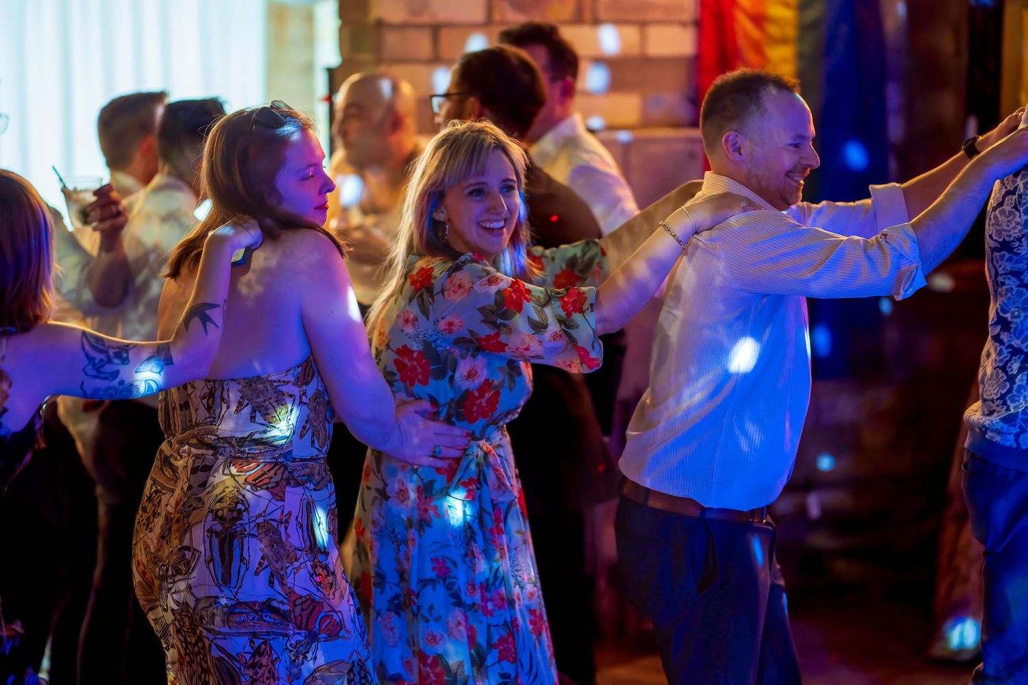 People dancing joyfully at a festive party, wearing glowing LED lights, in a warmly lit venue.