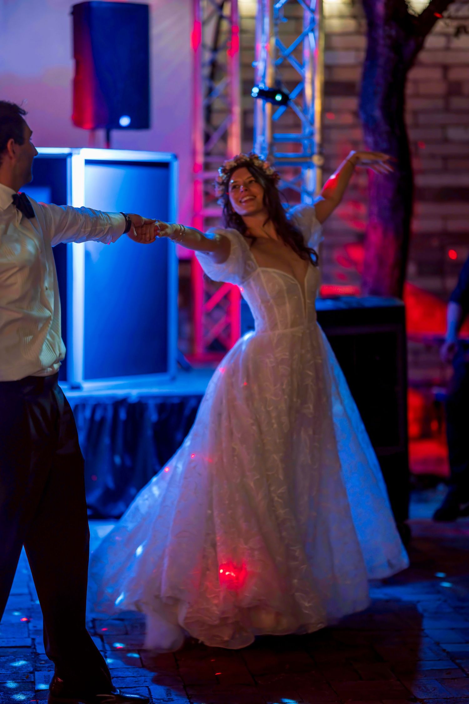 Bride in white ball gown dancing with groom under colorful blue and red lights at wedding reception.