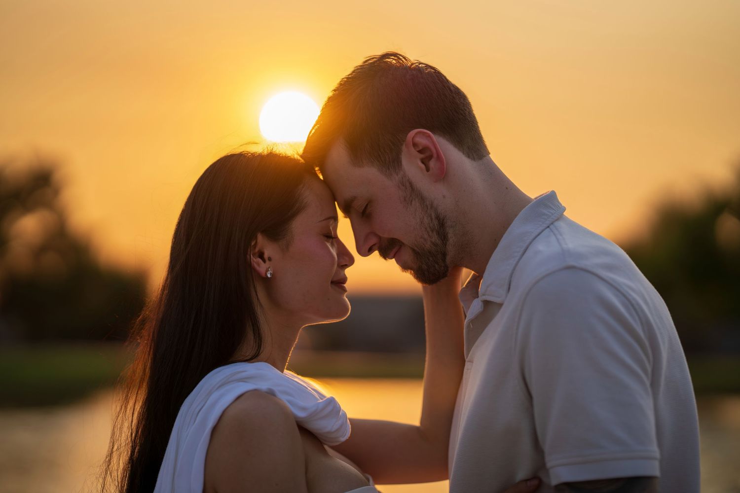 Romantic couple touching foreheads tenderly with a glowing golden sunset behind them.
