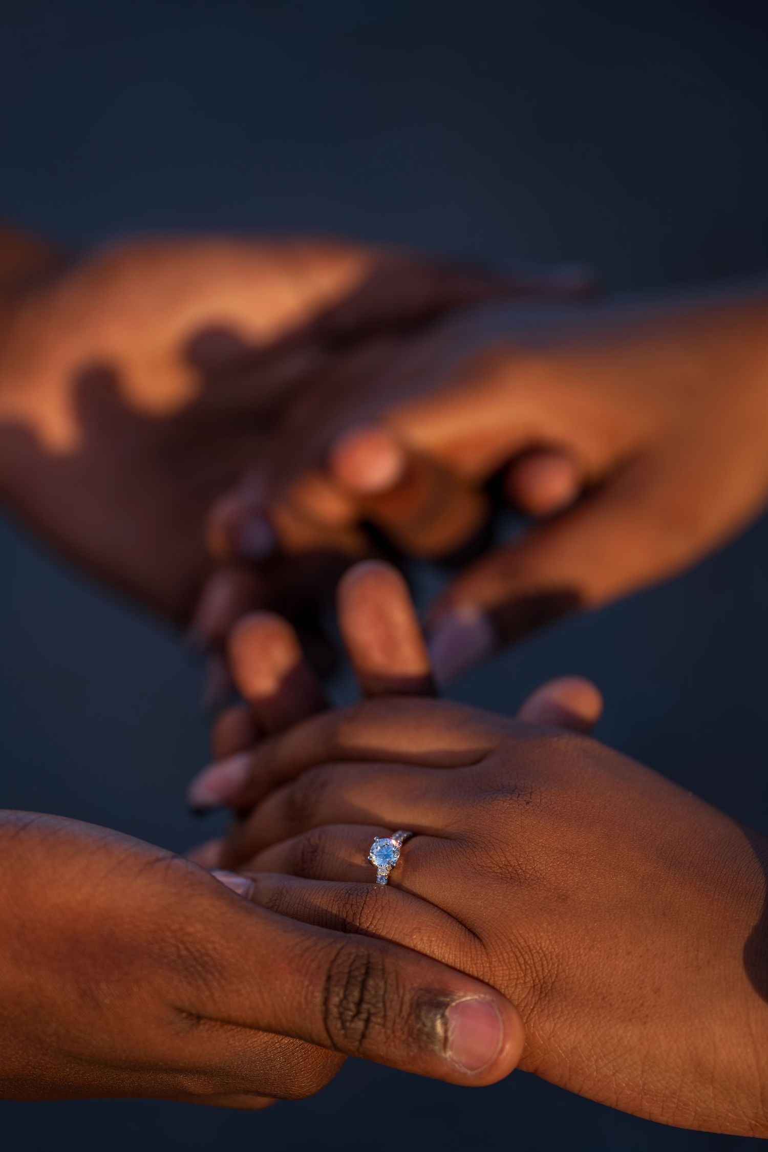 Romantic close-up of hands showing diamond engagement ring in warm golden light during proposal.