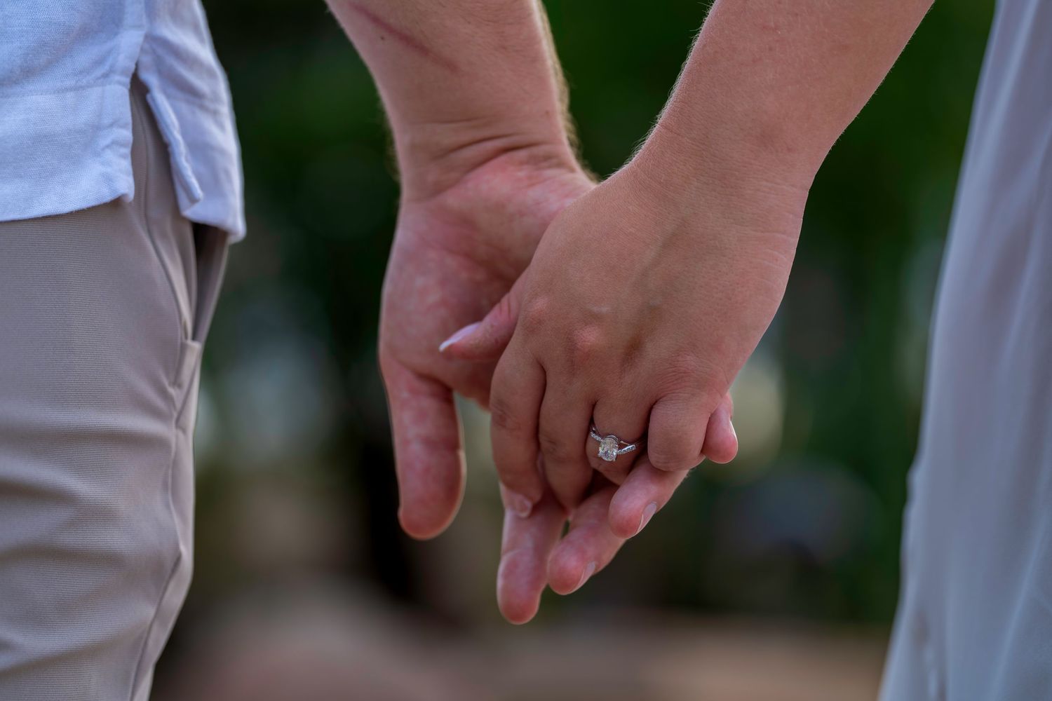 Close-up of a couple holding hands, showcasing a sparkling diamond engagement ring.