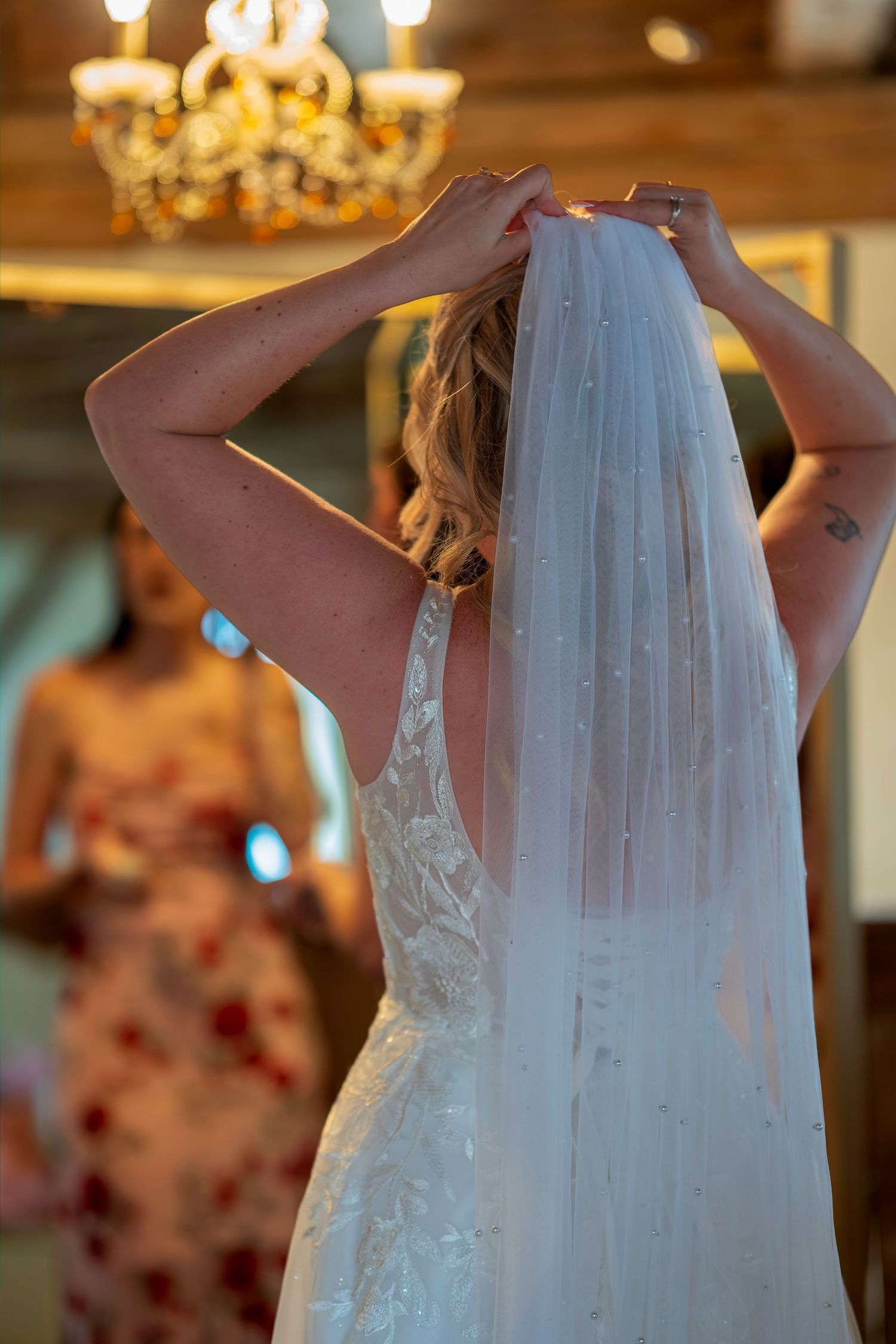 Bride adjusting her pearl-embellished wedding veil in a warmly lit bridal suite.