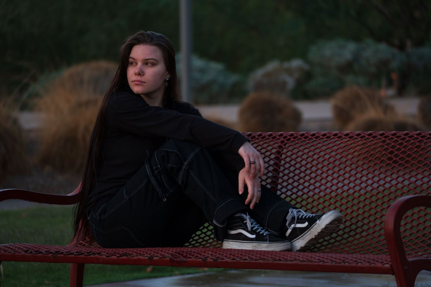 Relaxed pose on red bench during golden hour with dark clothing creating contrast.