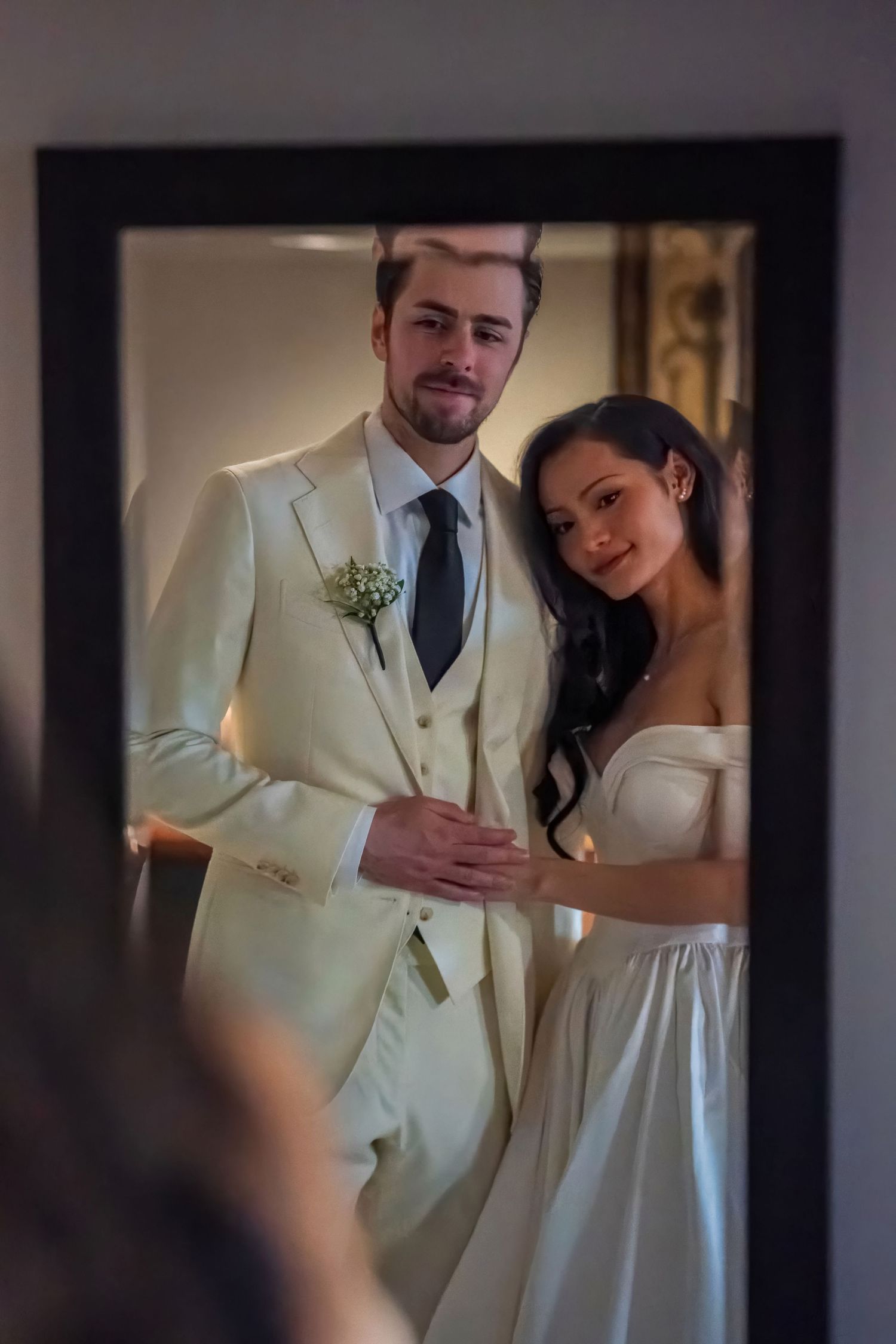 A wedding couple poses for a mirror reflection shot in formal attire.
