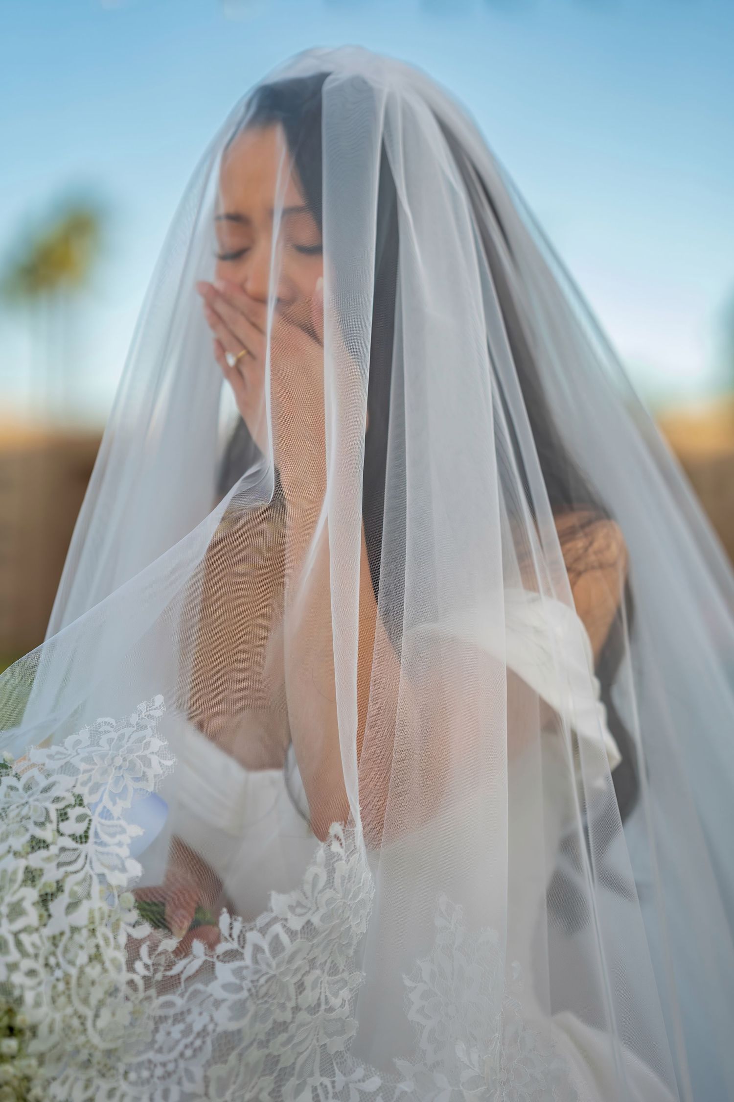 An intimate bridal portrait capturing a candid emotional moment through a sheer veil.