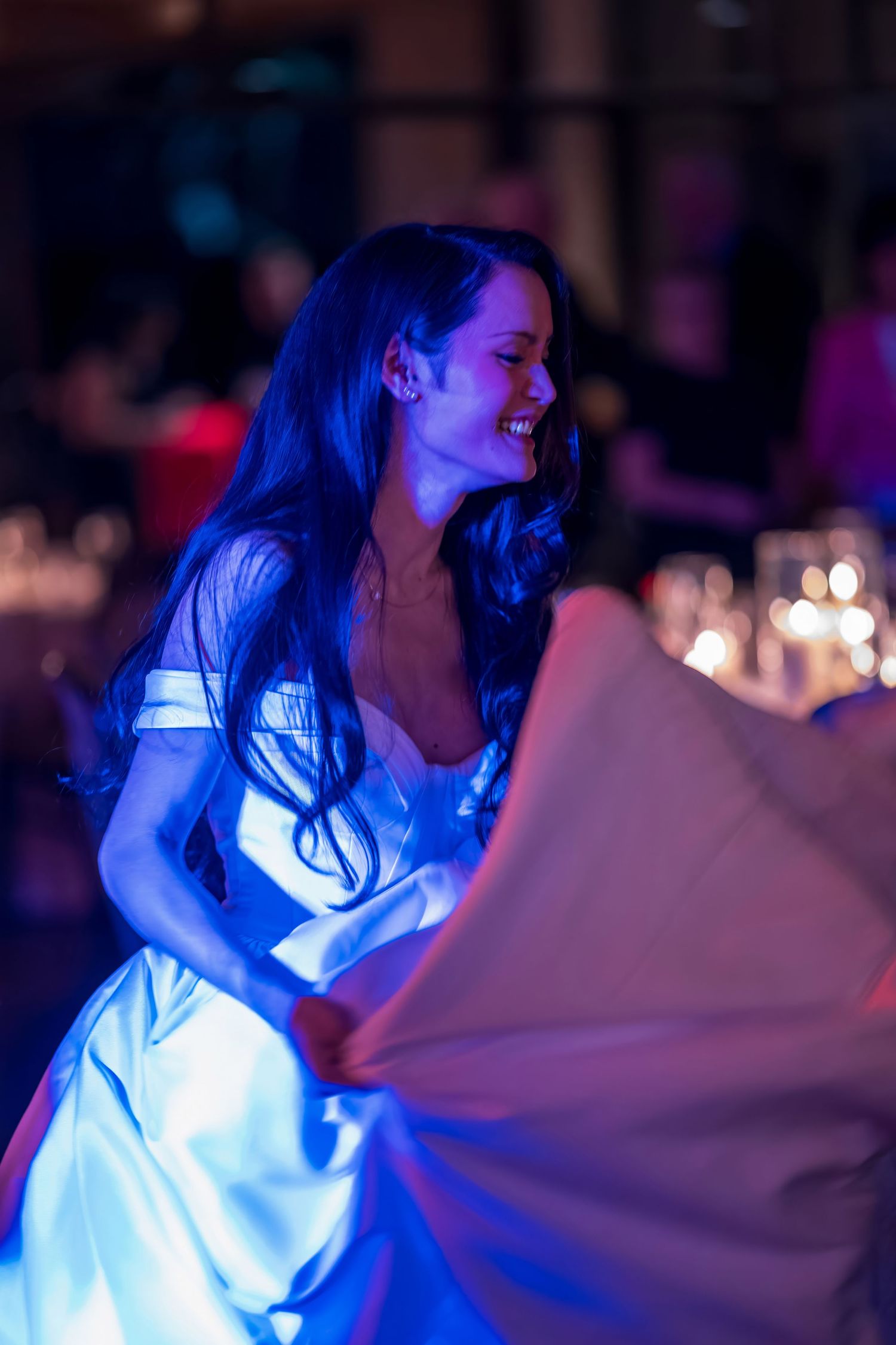 Woman in flowing white dress twirls on dance floor under dramatic blue lighting.