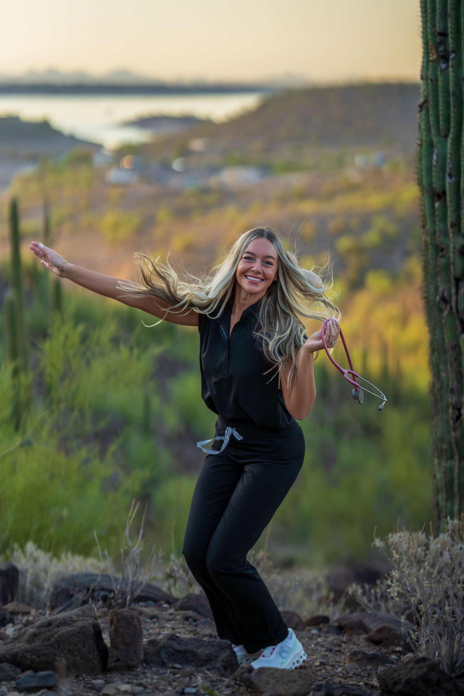 Healthcare worker dances playfully in black scrubs against scenic desert mountain backdrop.