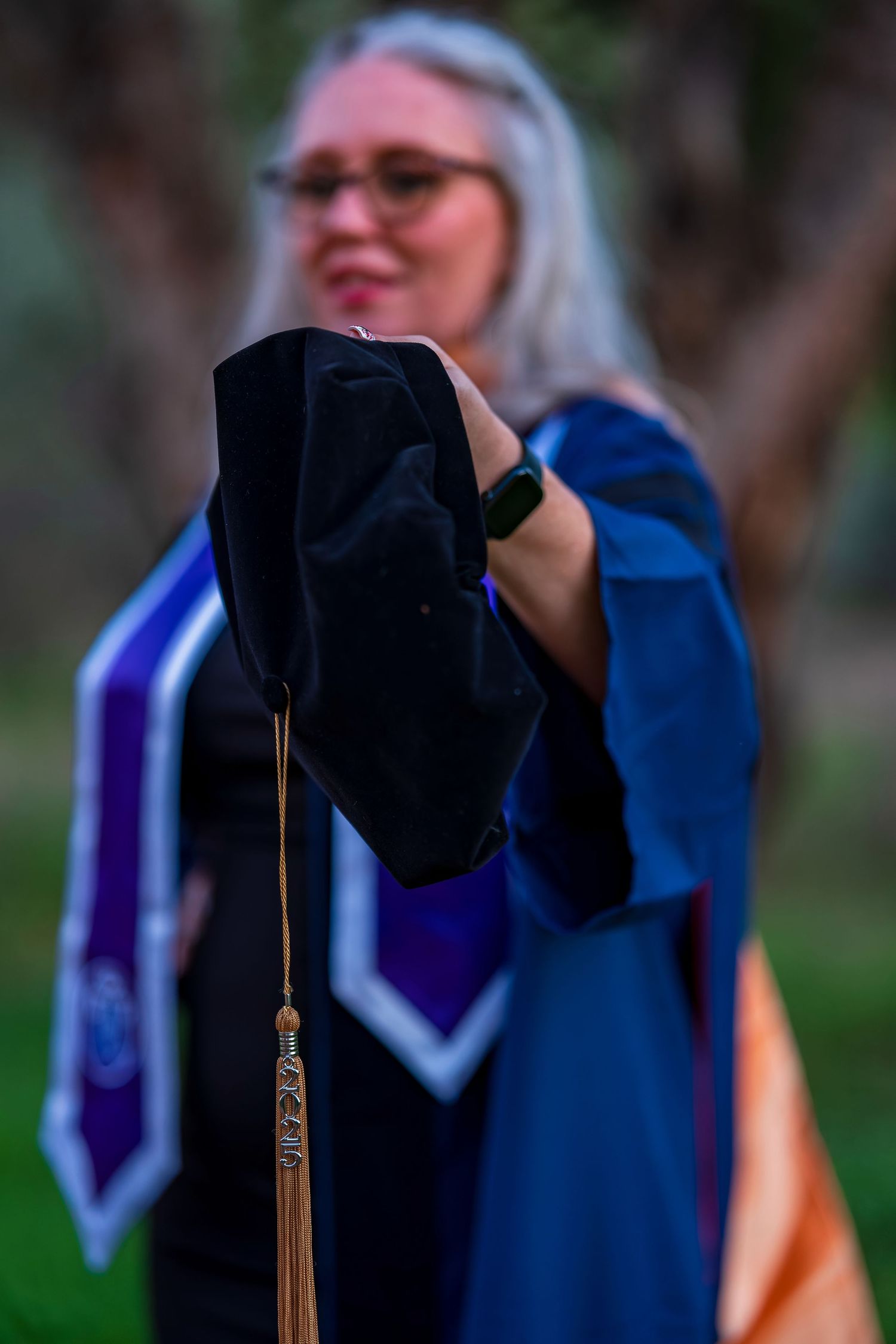 Close-up of graduation cap with tassel being held up against blue academic regalia.
