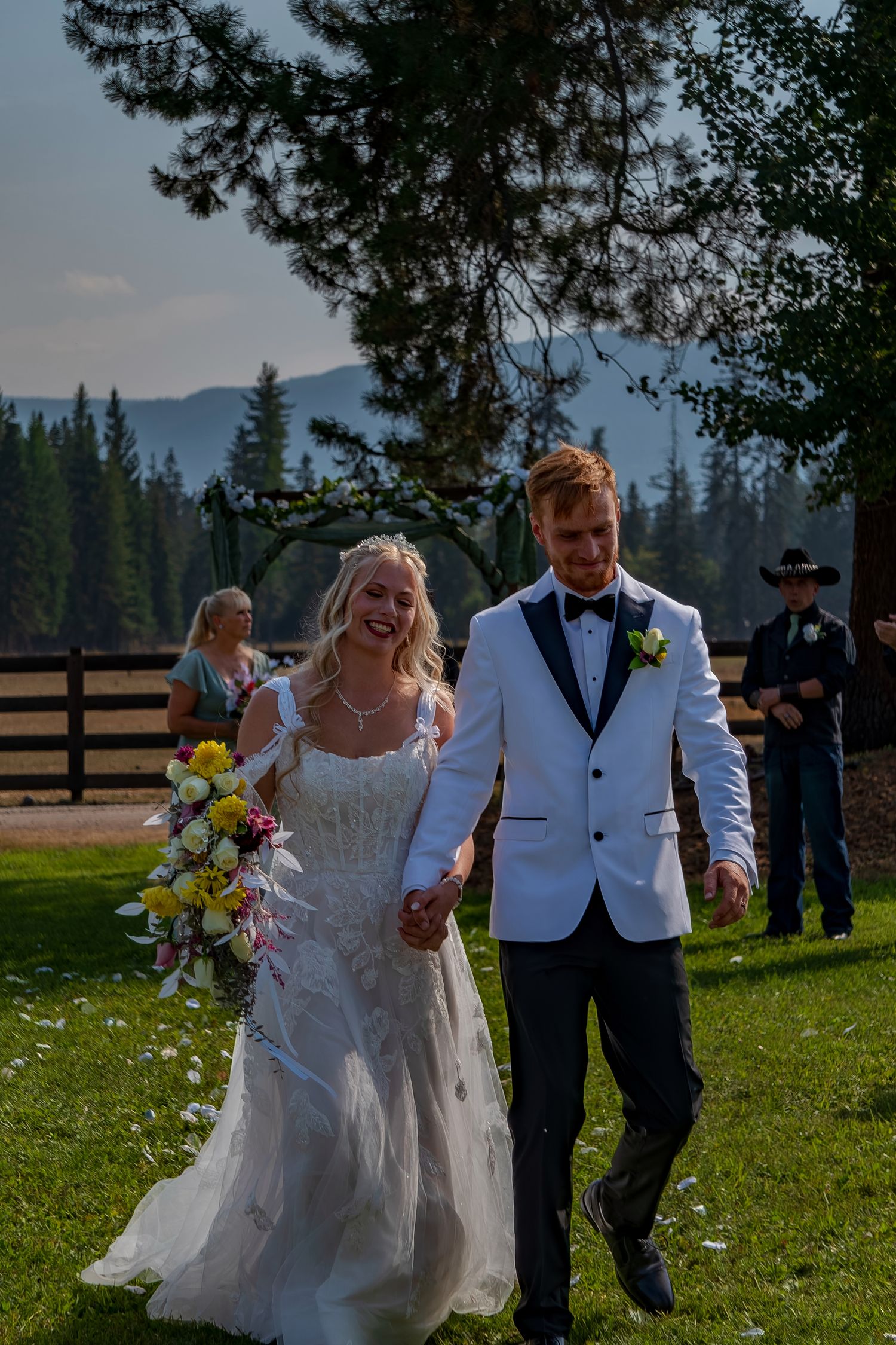 Joyful newlyweds walking together on grassy field with mountain landscape behind them.