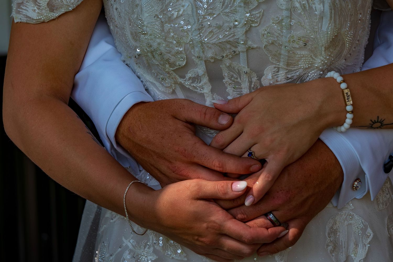 Close-up of hands wearing wedding rings in a romantic pose.