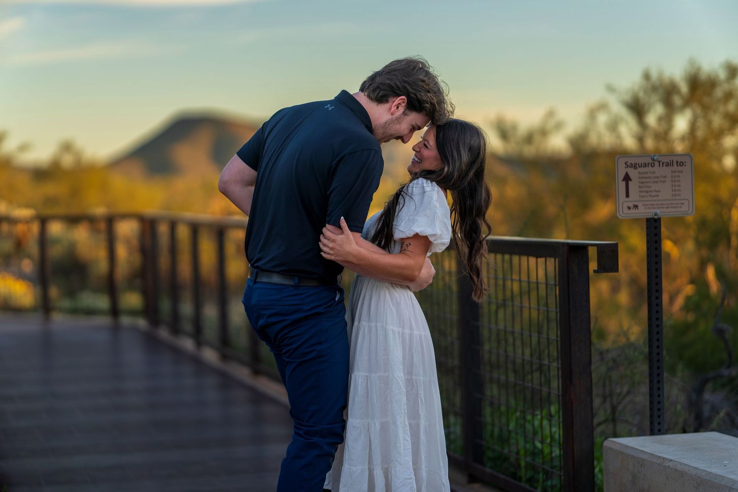 A couple shares an intimate moment at sunset on a desert overlook with mountains in the background.