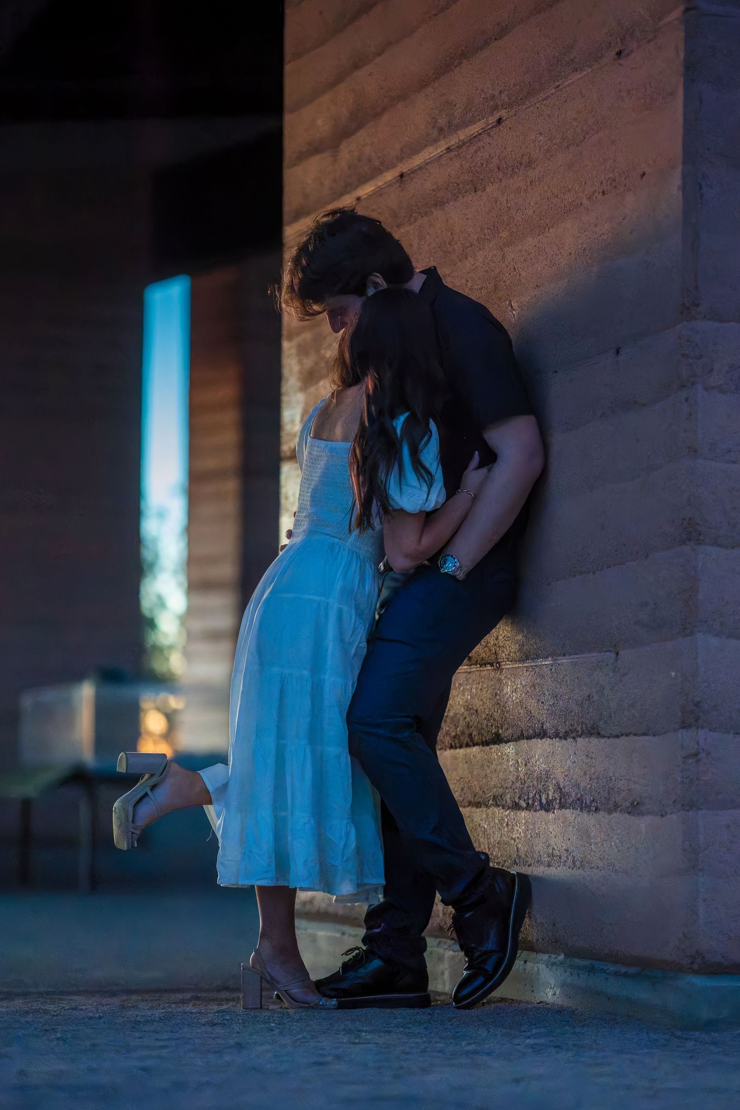 Silhouetted couple shares tender moment against illuminated wall at dusk.