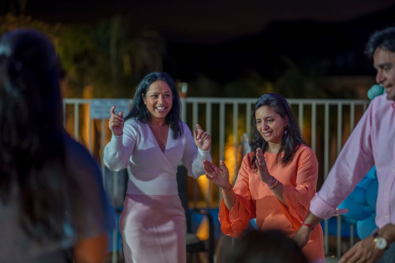People dancing and celebrating at a party with colorful balloon decorations in the background.