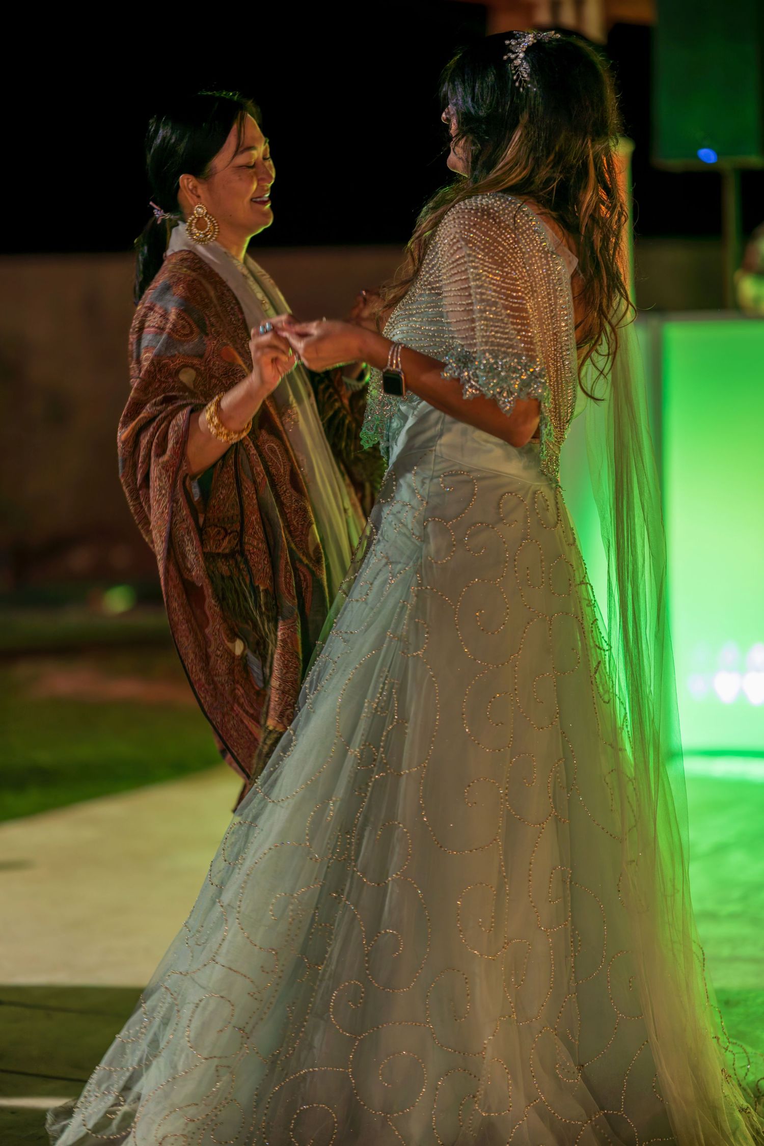 Two people in formal attire dance under green lighting at an event.