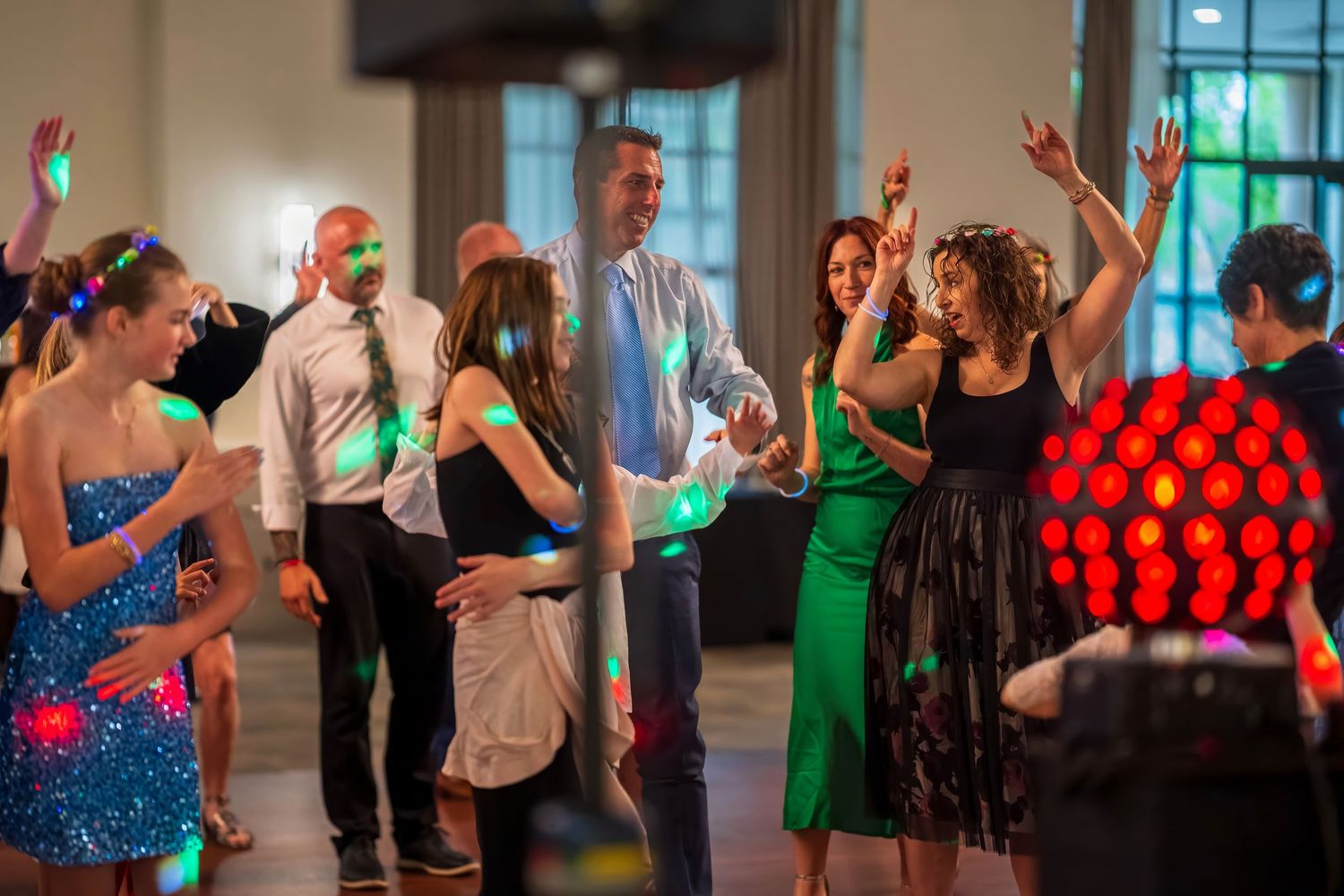 Guests dancing joyfully under colorful disco lights at a lively indoor party or wedding reception.