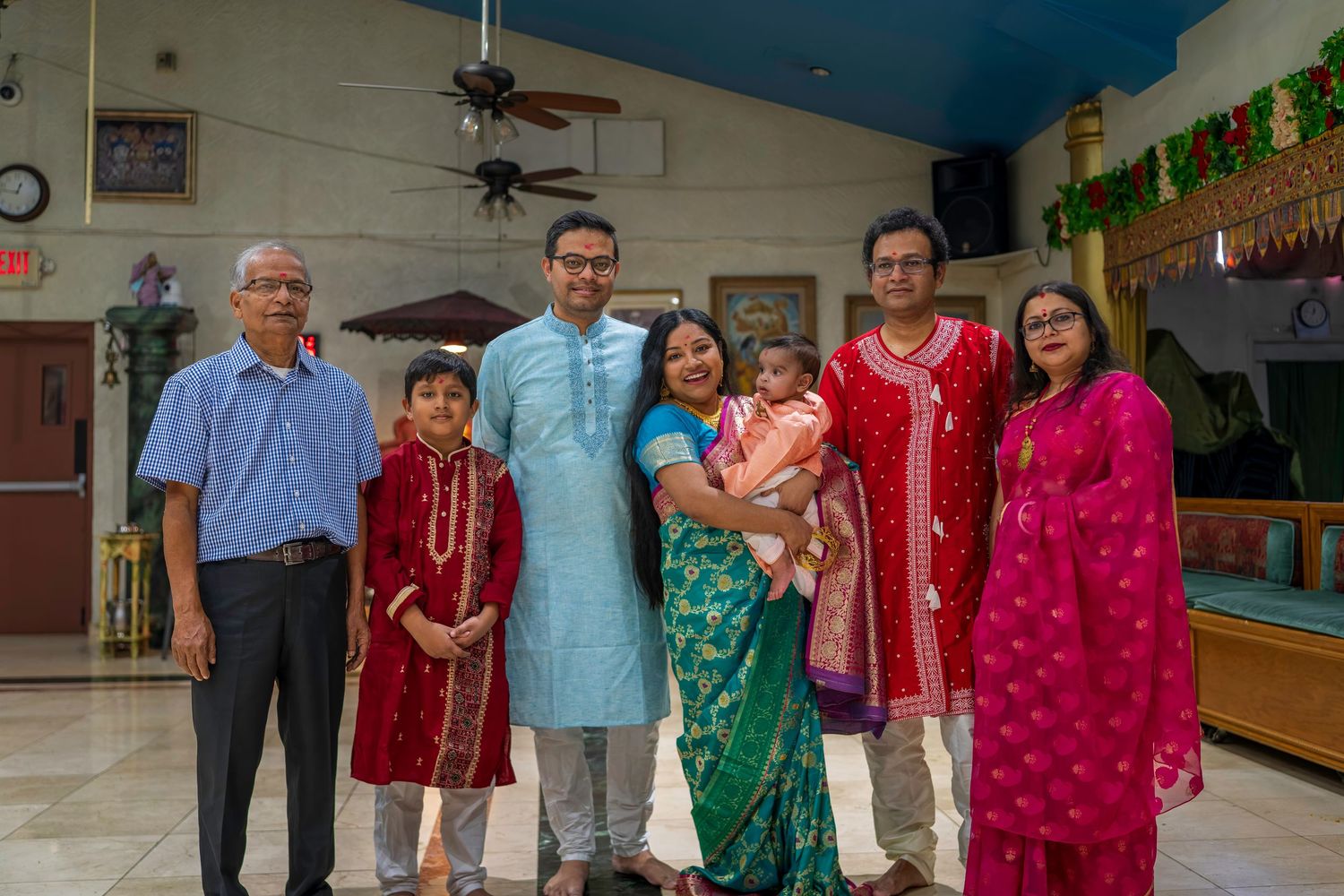 Indian family group portrait in colorful traditional clothing at decorated indoor venue.