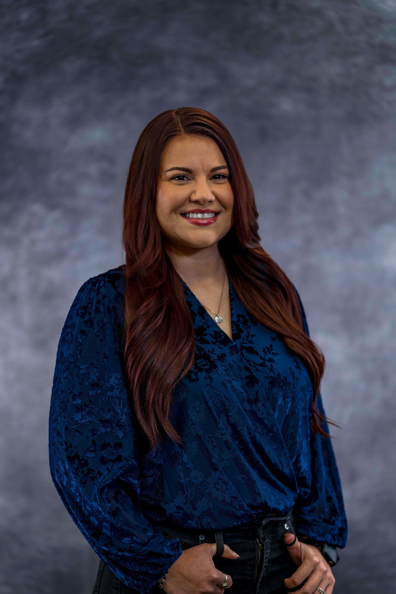 Professional portrait of woman in dark blue velvet top against gray backdrop.