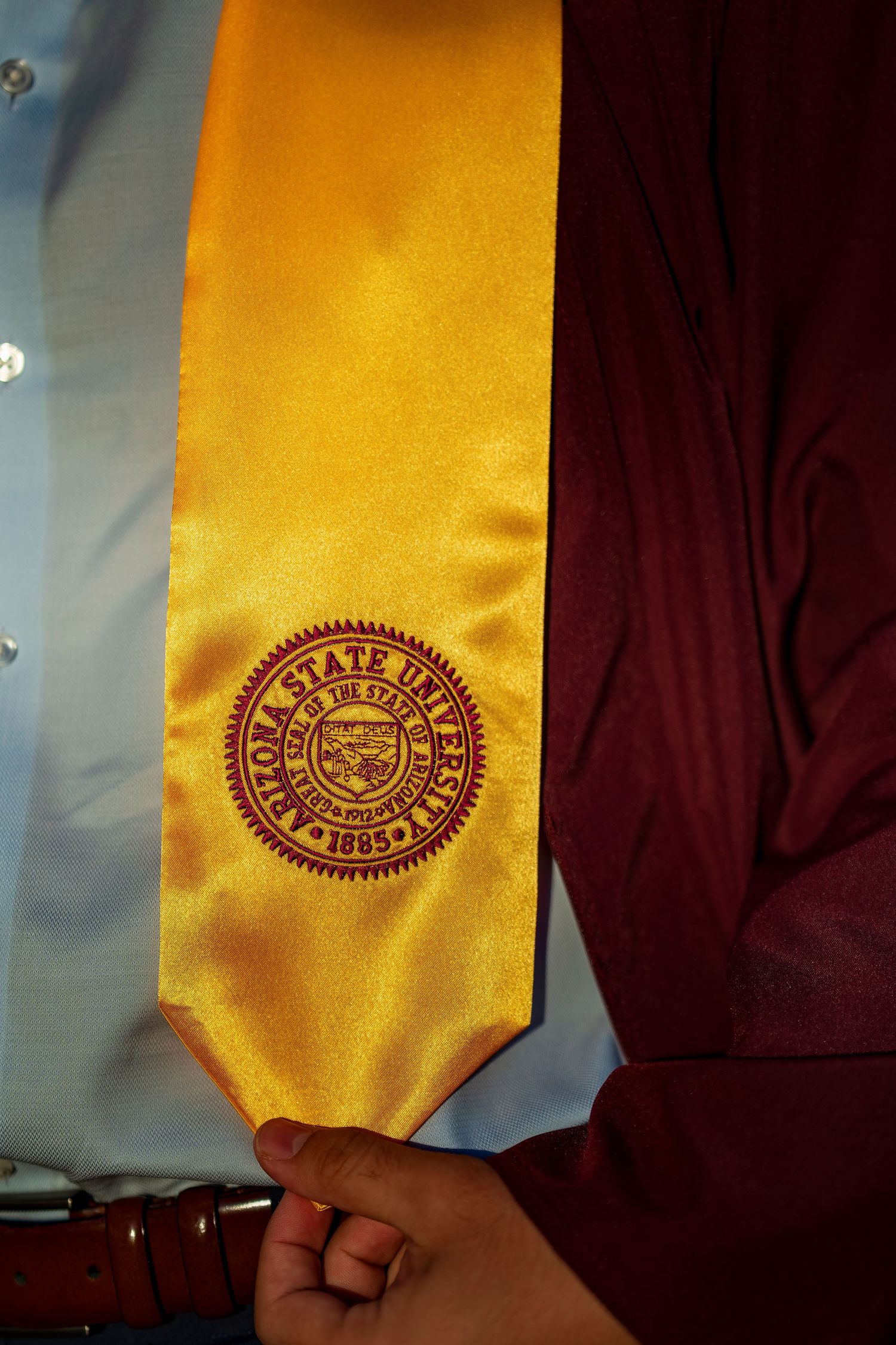 Close-up of gold graduation stole with university seal embroidered in maroon.