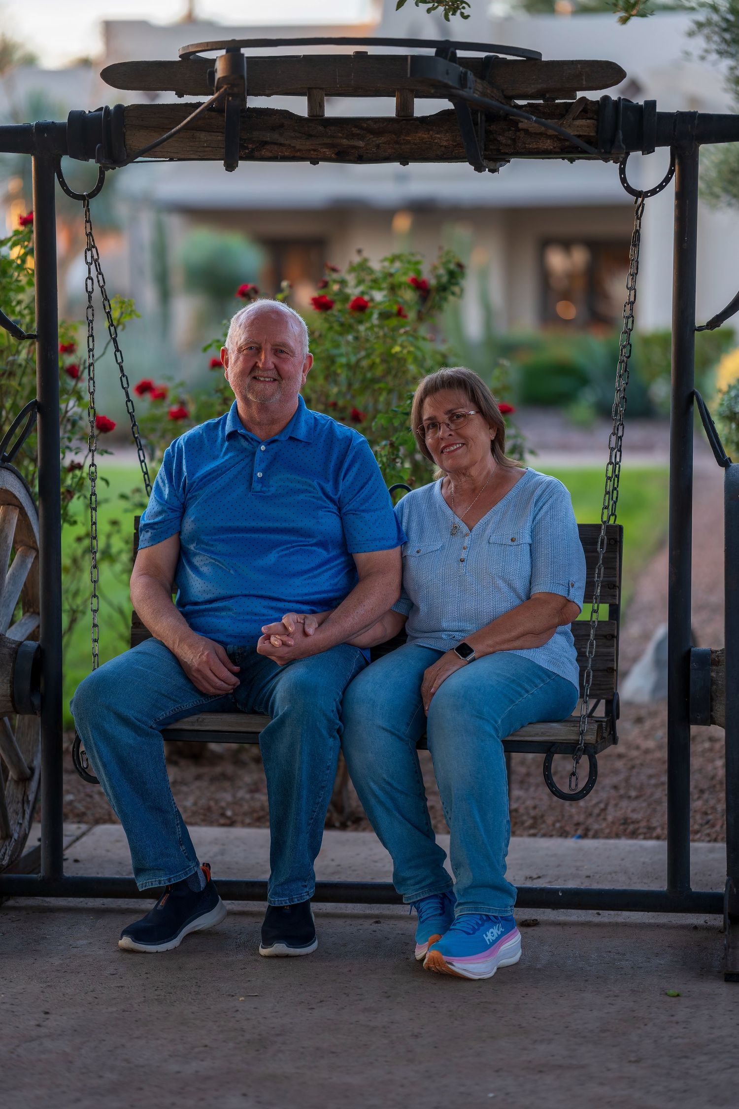 Couple sits together on a wooden porch swing in a garden setting at dusk.