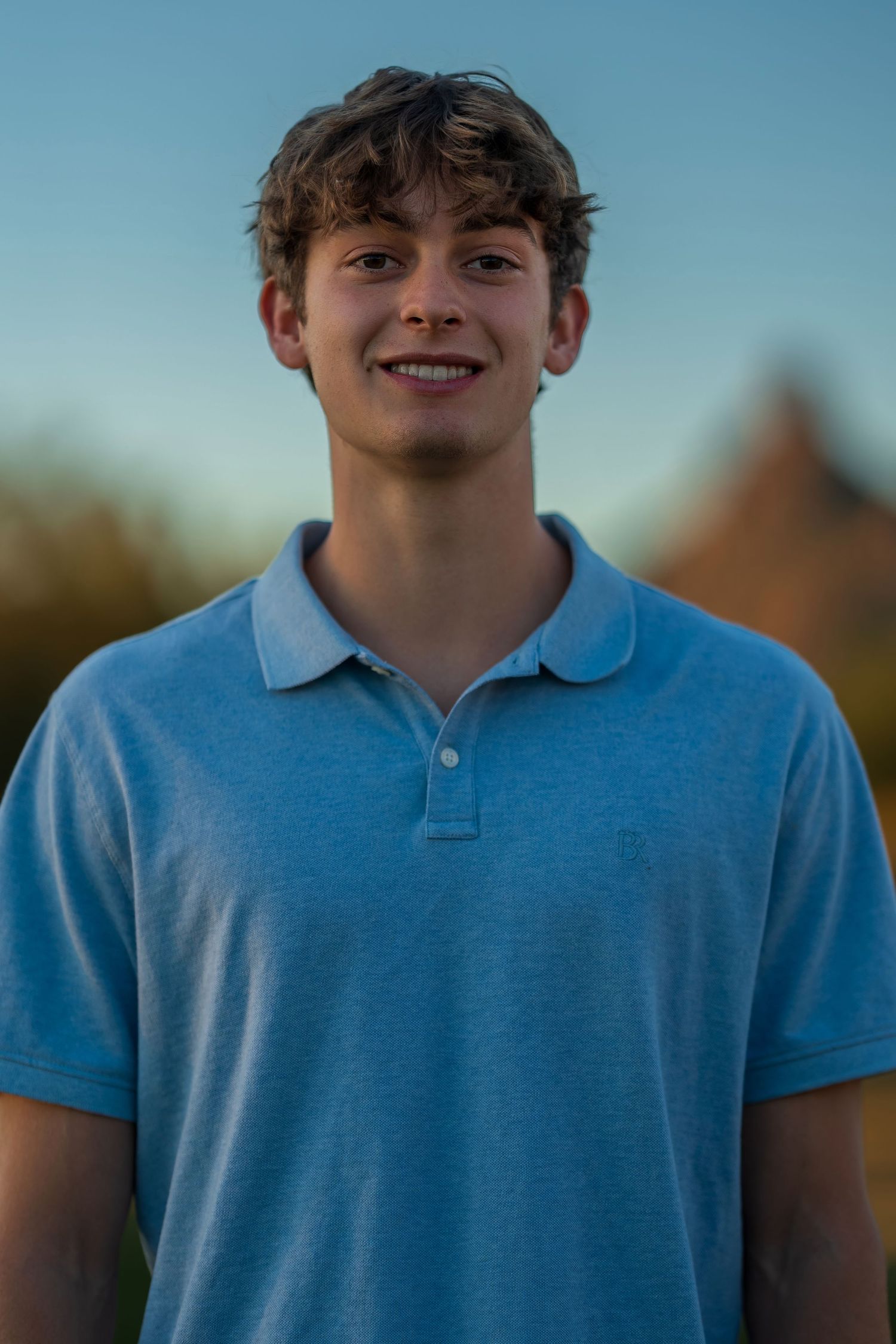 Portrait of person wearing light blue polo shirt outdoors at sunset.
