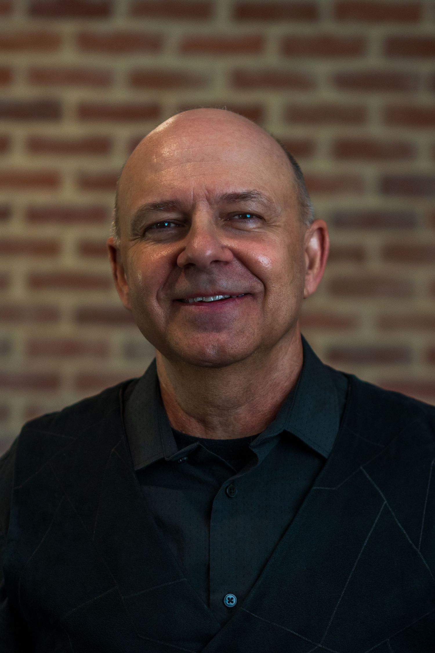 Close-up portrait against a brick wall showing a warm expression.