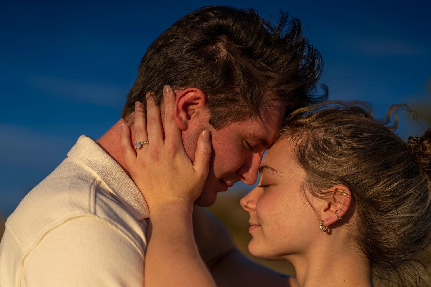 Romantic couple touching foreheads with eyes closed under a vivid blue sky.