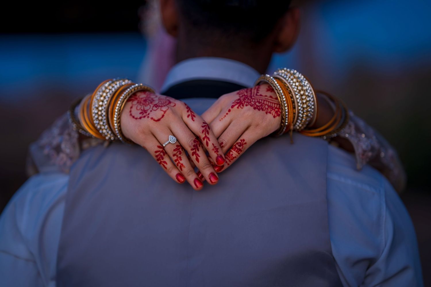 Bride with henna mehndi hands and gold bangles clasped around grooms suit jacket.