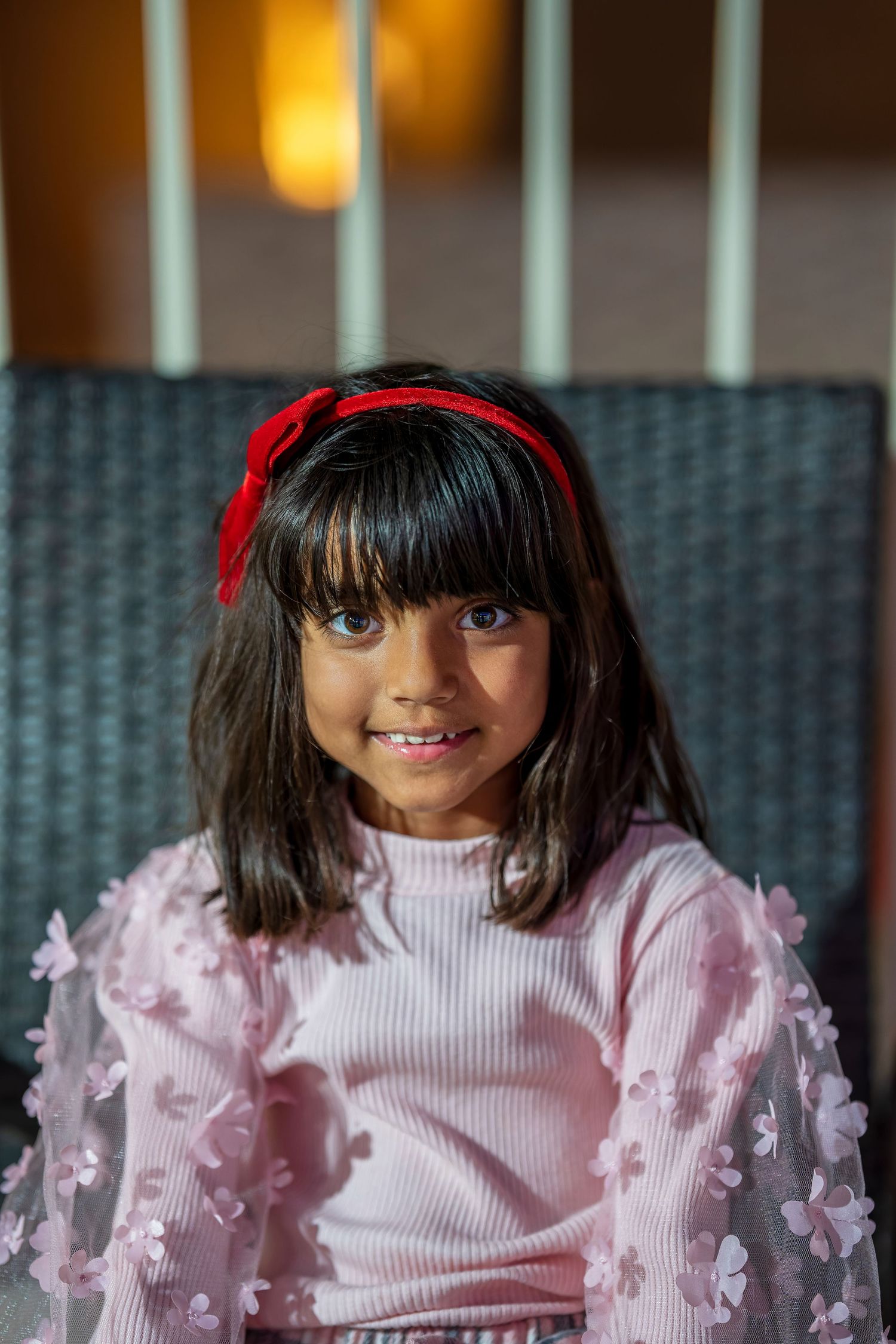 A decorative doll with bangs wears a pink ruffled dress and red hair accessory.