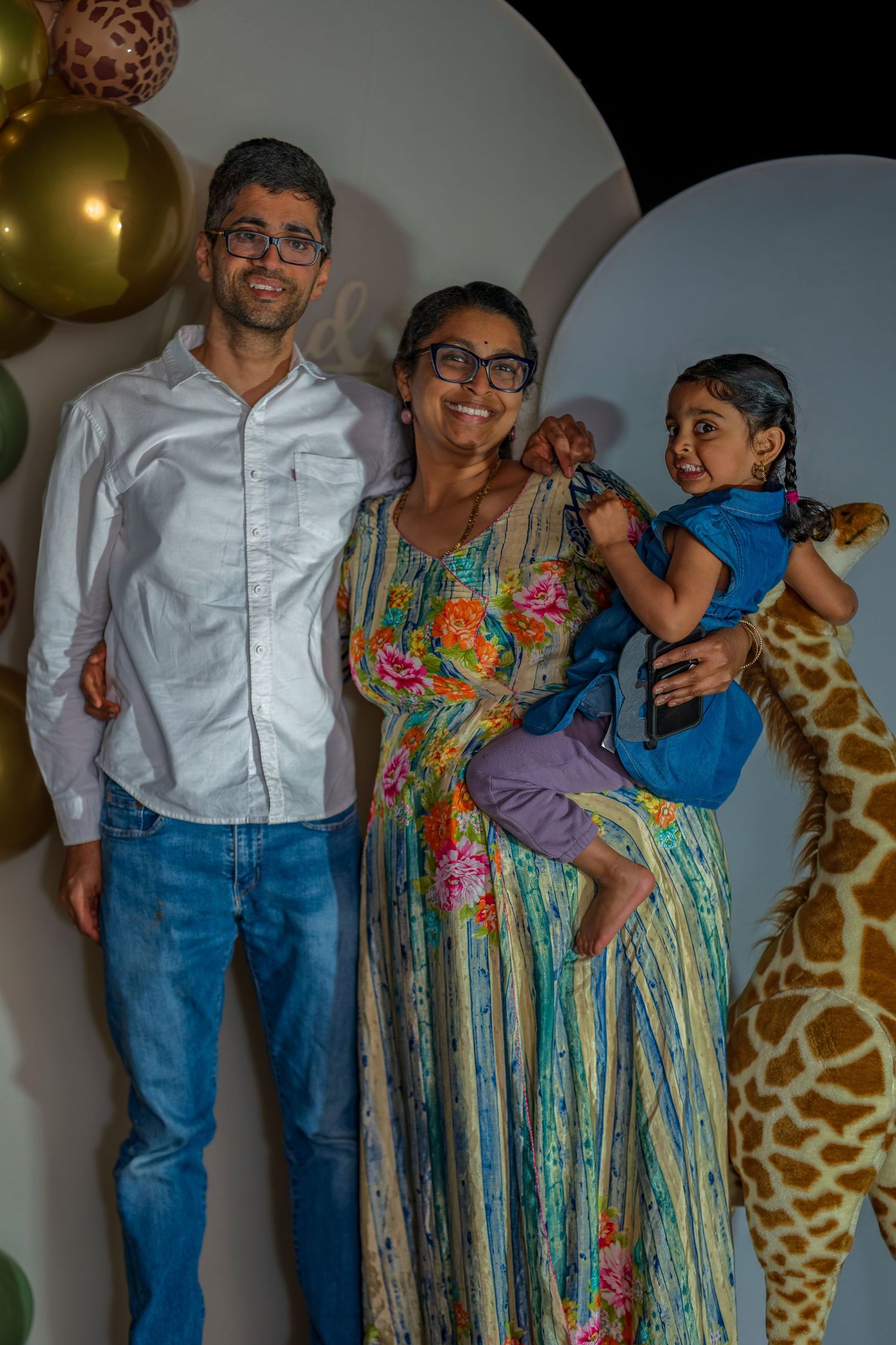 A family poses together at a party with decorative balloons and a giraffe prop.