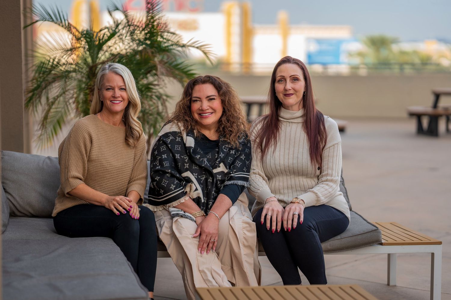 Friends relaxing and laughing together on an outdoor patio with palm trees in background.