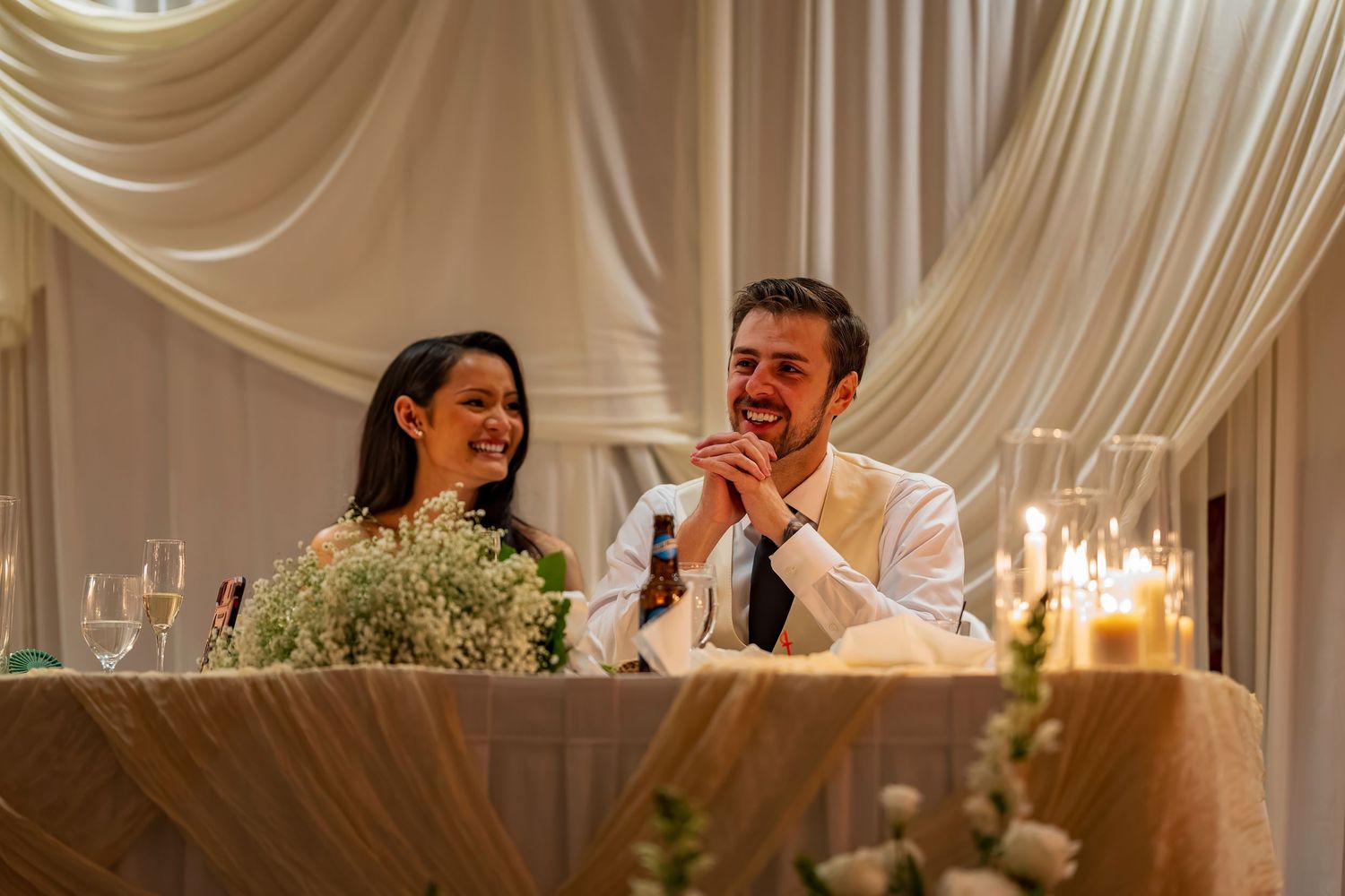 Wedding reception venue with white draped ceiling and elegant candlelit table settings.