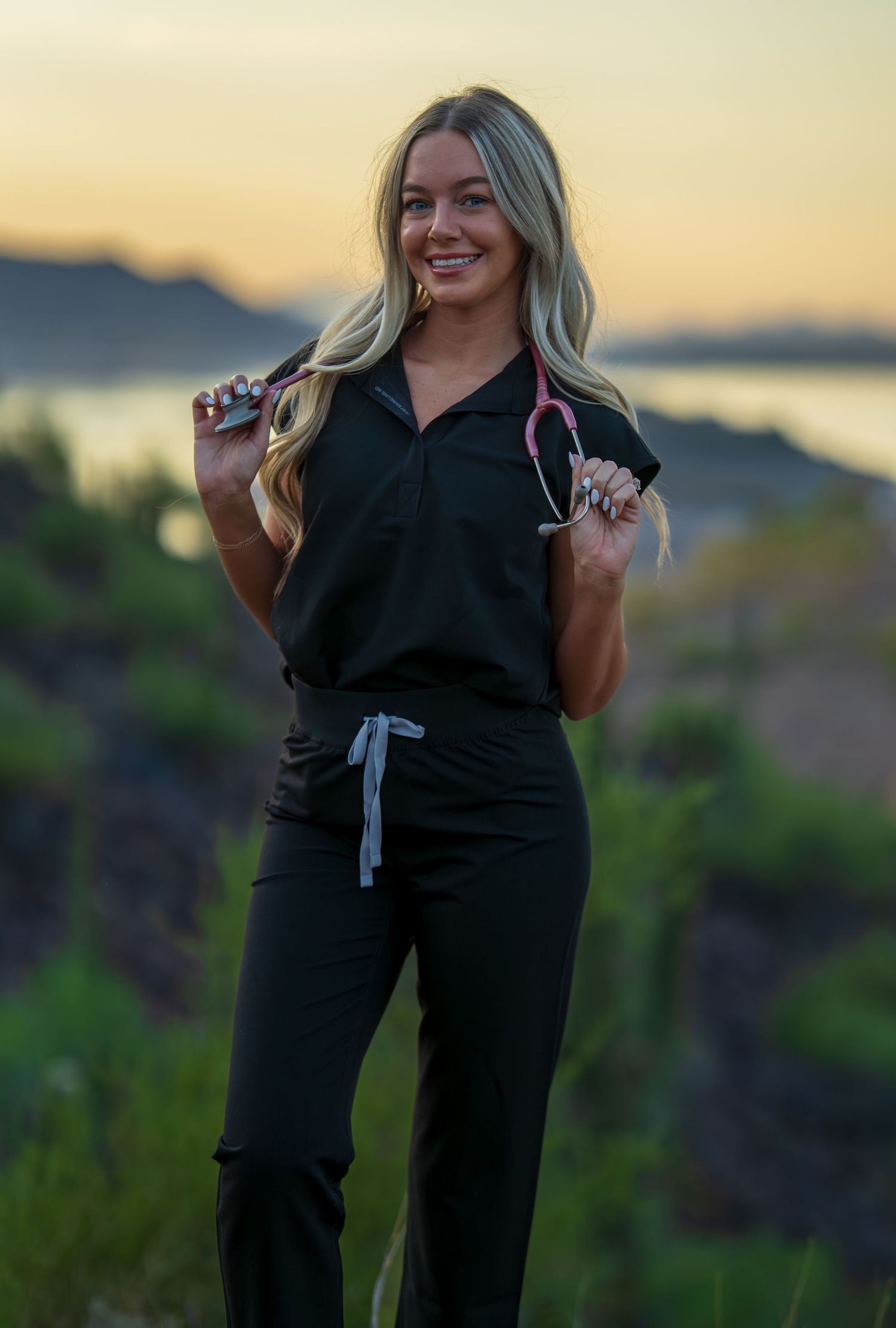 Medical professional holding stethoscope stands on desert hillside during sunset.