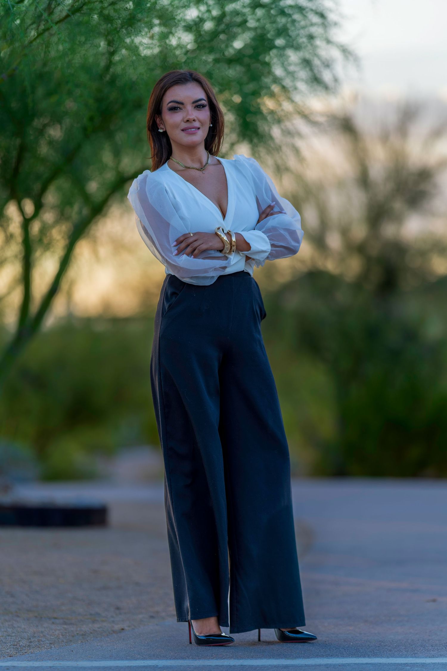 Elegant woman in white blouse and black wide-leg trousers posing outdoors at sunset.