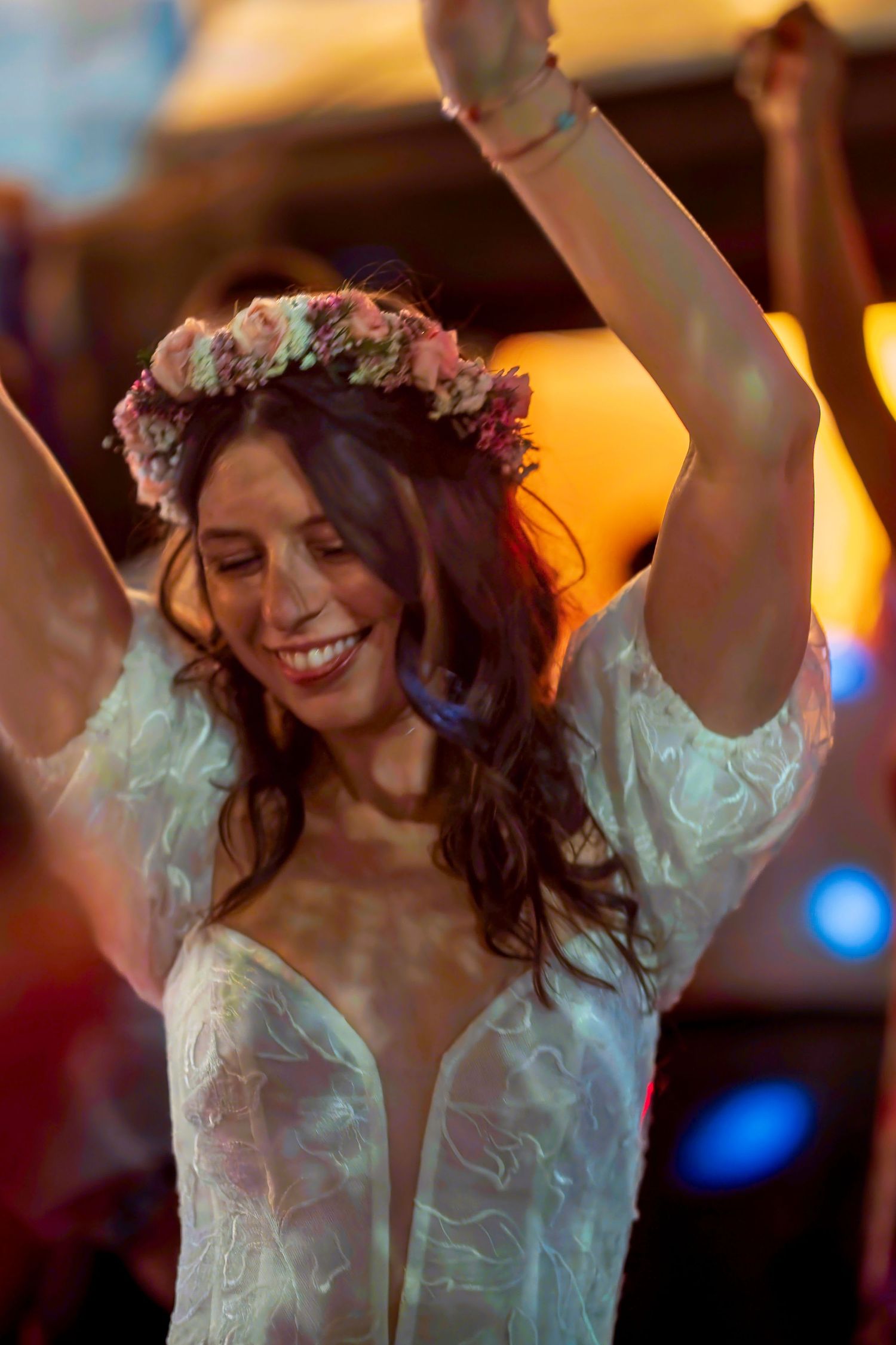 Joyful bride with floral crown dancing with arms raised, smiling at outdoor wedding celebration.