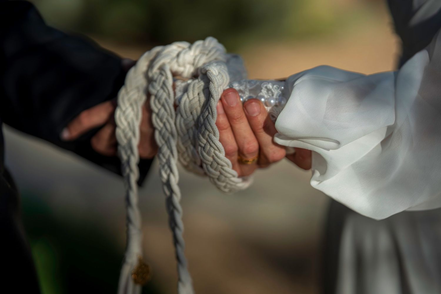 Close-up of bride and groom hands bound together with white rope during a unity cord wedding ceremony.