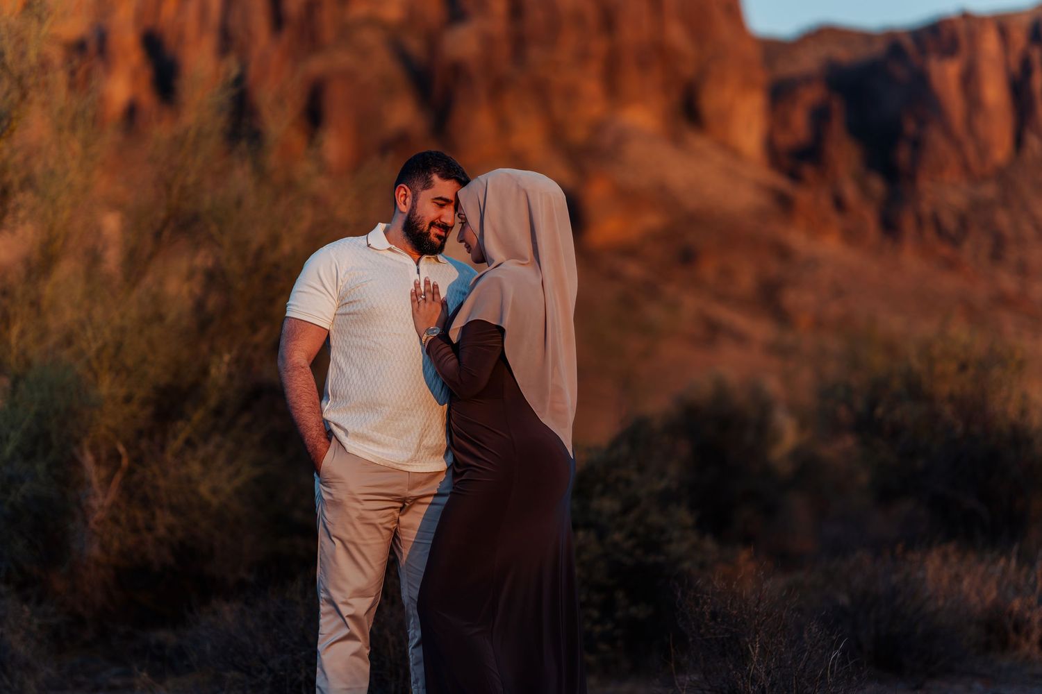 Couple sharing a romantic moment at golden hour with red rock formations in the desert background.