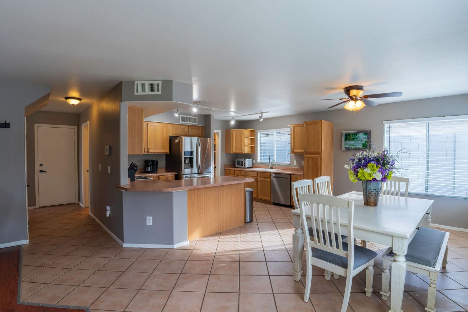 Spacious open-concept kitchen and dining area with tile floors, wood cabinets, stainless appliances, and a white dining set.
