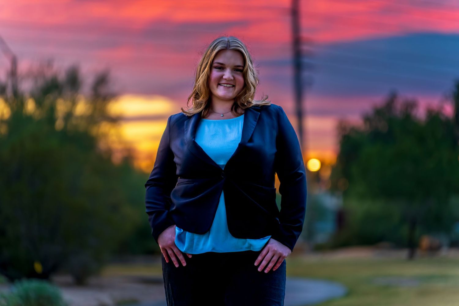 Figure stands dramatically against a vibrant pink and purple sunset sky wearing business attire.