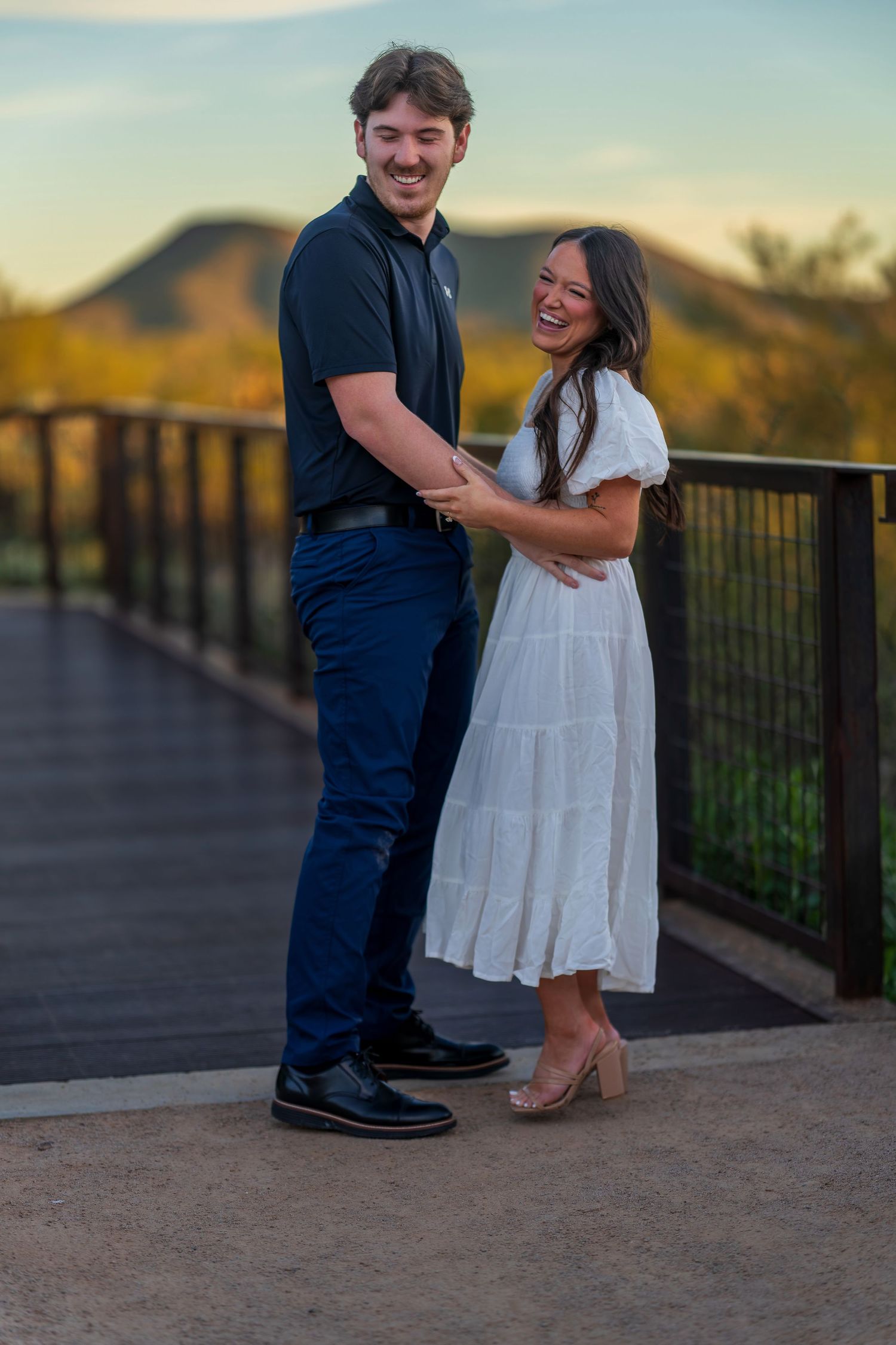 A joyful moment captured between two people on a desert overlook during sunset.