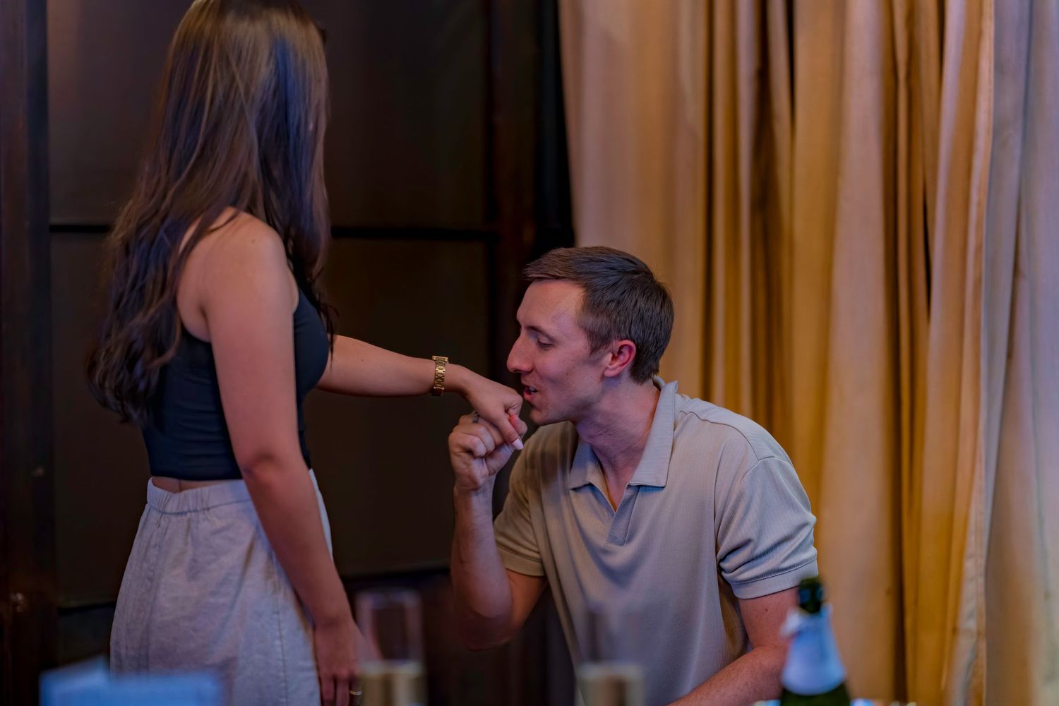 A romantic moment captured as a couple shares an intimate gesture at a dimly lit restaurant.