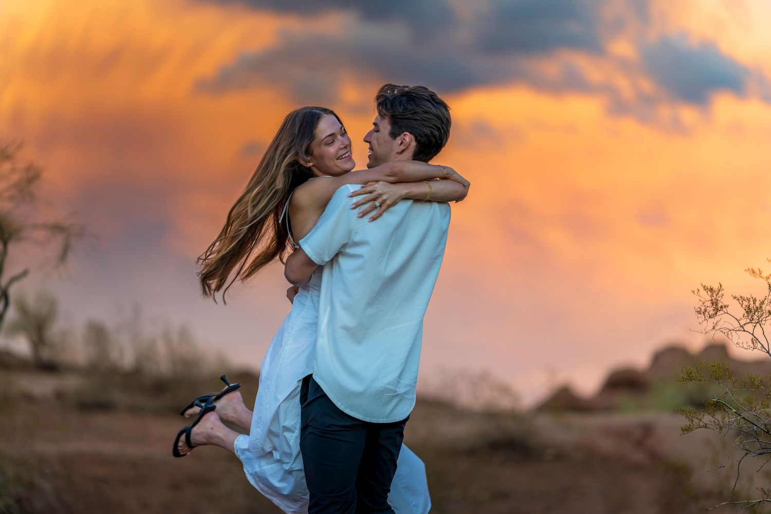Playful couple dancing and laughing together during a vibrant sunset photoshoot.